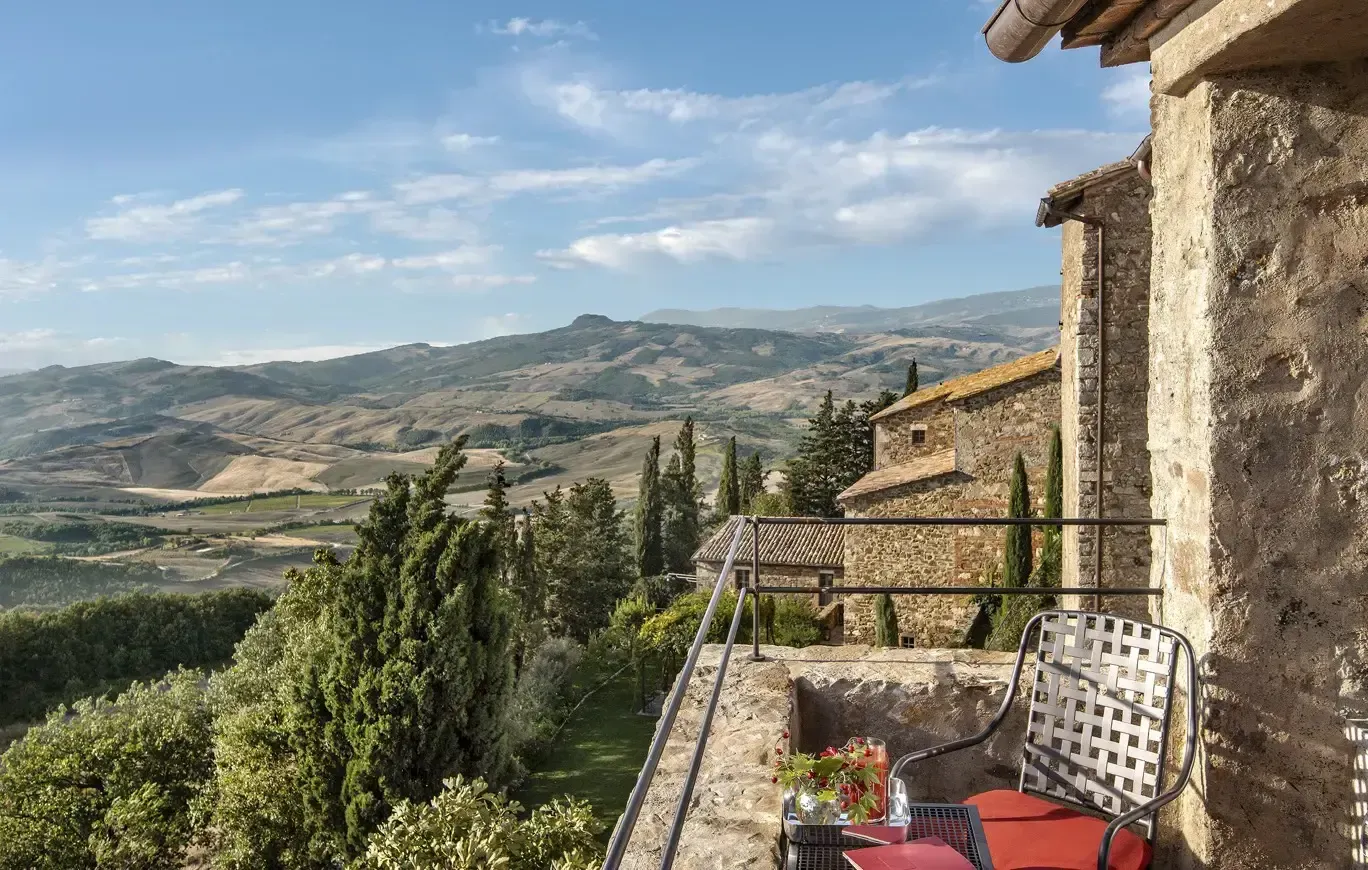 Monteverdi, Tuscany, Italy — Stone terrace overlooking rolling hills, cypress trees, weathered architecture, afternoon light, rustic luxury aesthetic.