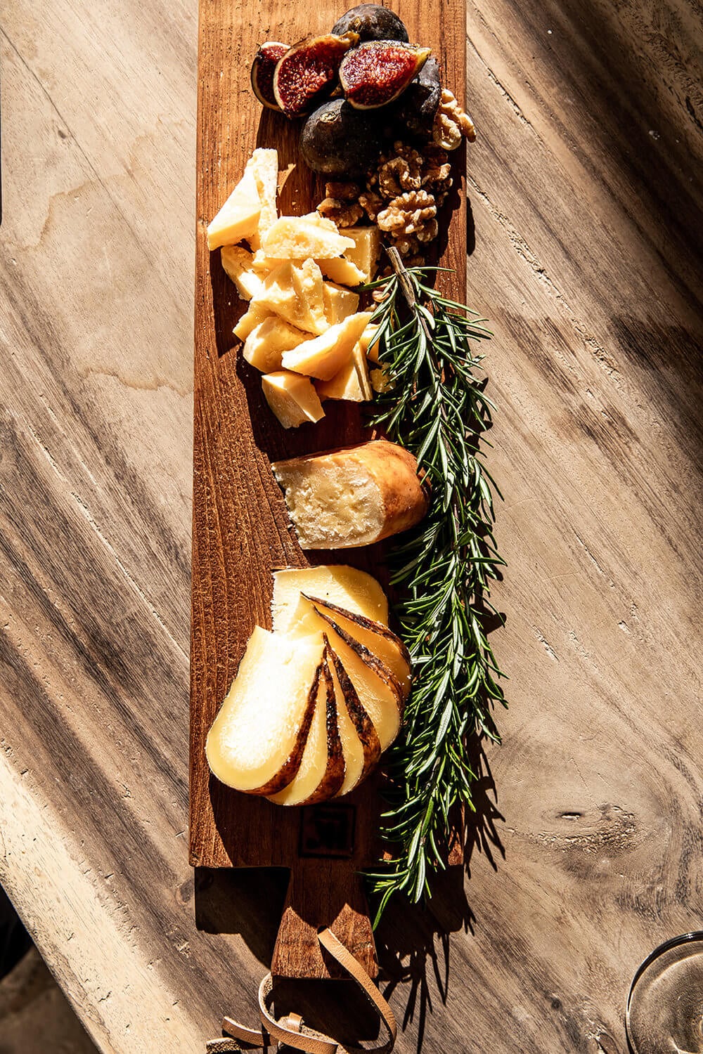 Lunch with Xisco, Balearic Islands — Wooden charcuterie board with figs, walnuts, cured meats, cheese, and rosemary in Mediterranean sunlight.