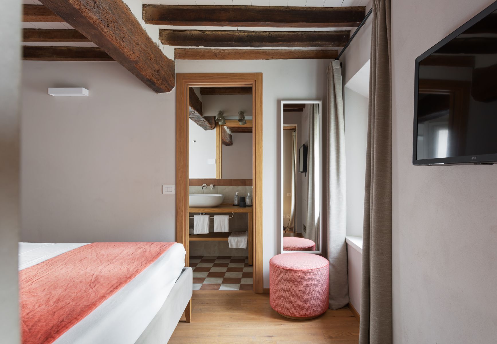 Roncolo 1888, Europe — Bedroom with exposed wooden beams, coral bedding, pink poufs, ensuite bathroom with vessel sink, and warm wood and tile finishes.
