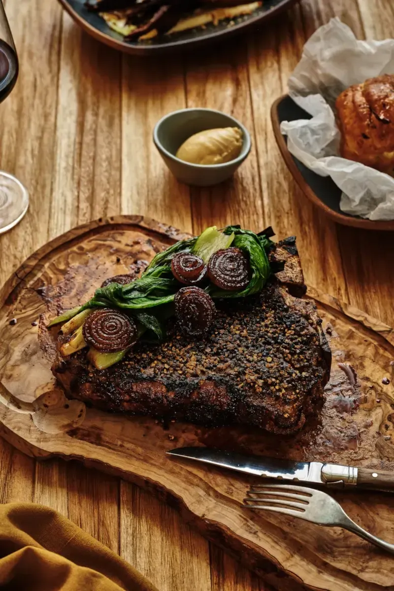 Wildflower Farms, North America — Grilled steak with roasted beets and charred greens on wooden serving board, candlelit fine dining presentation.