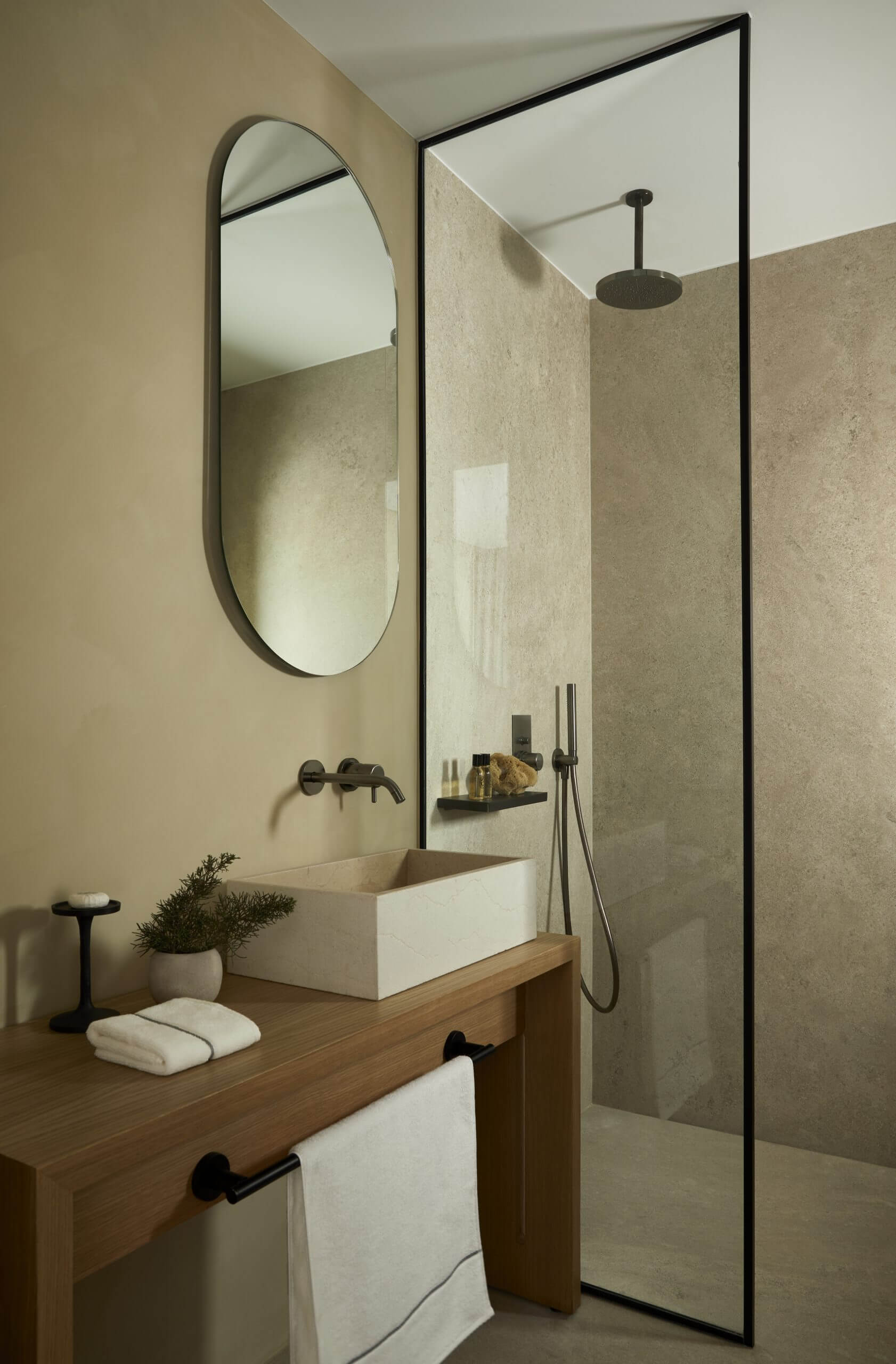 Pārocks, Europe — Minimalist bathroom with limestone walls, wooden vanity, white basin sink, black-framed mirror and glass shower enclosure, matte black fixtures.