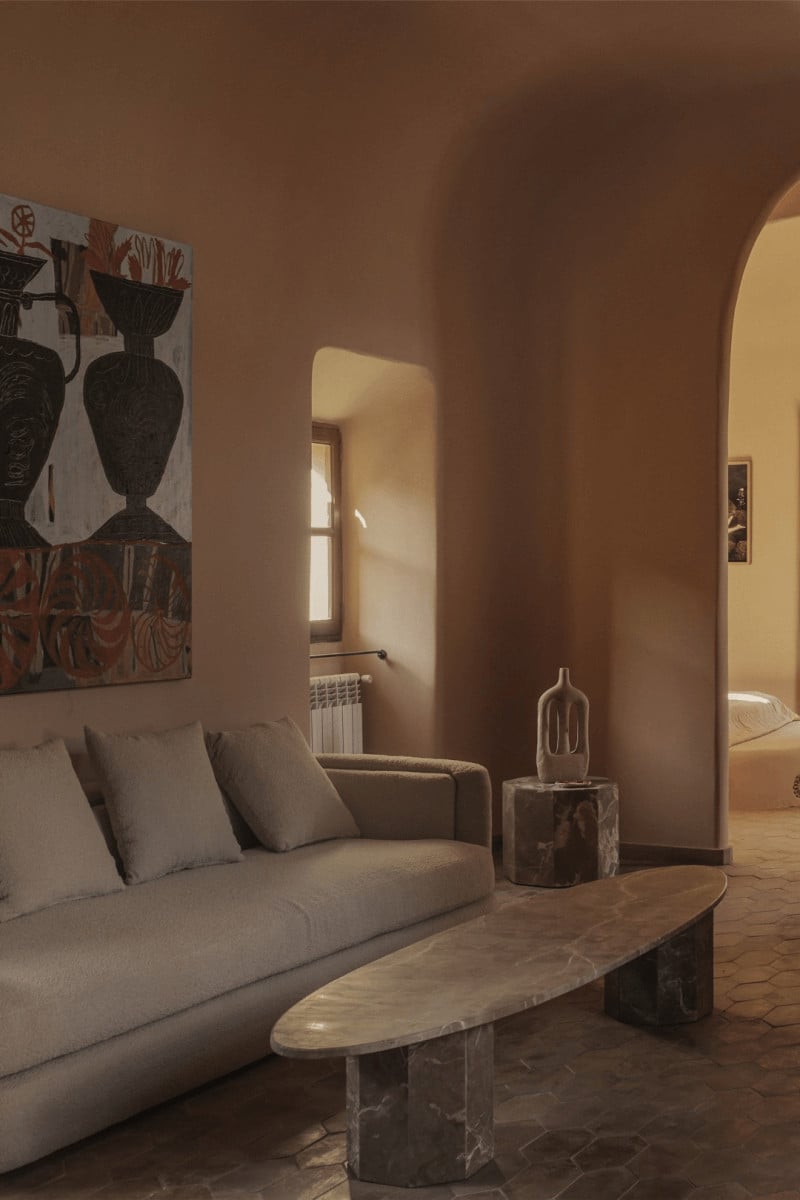 Hotel Corazón, Balearic Islands, Spain — Terracotta living room with curved archways, minimalist furnishings, marble coffee table, and warm natural light casting geometric shadows on earth-toned walls.