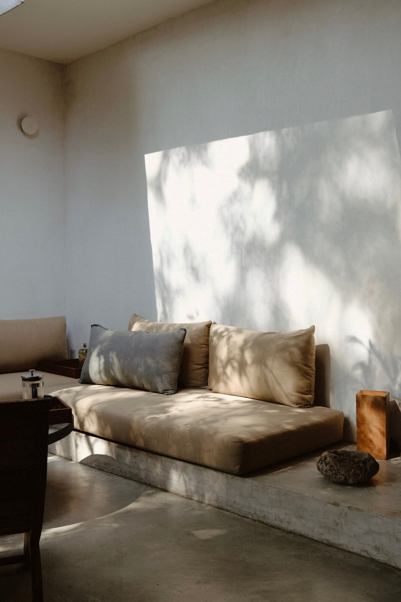 Casa Criollo, Mexico — Minimalist daybed with neutral cushions bathed in natural light, concrete platform, white walls, and sculptural stone accent.
