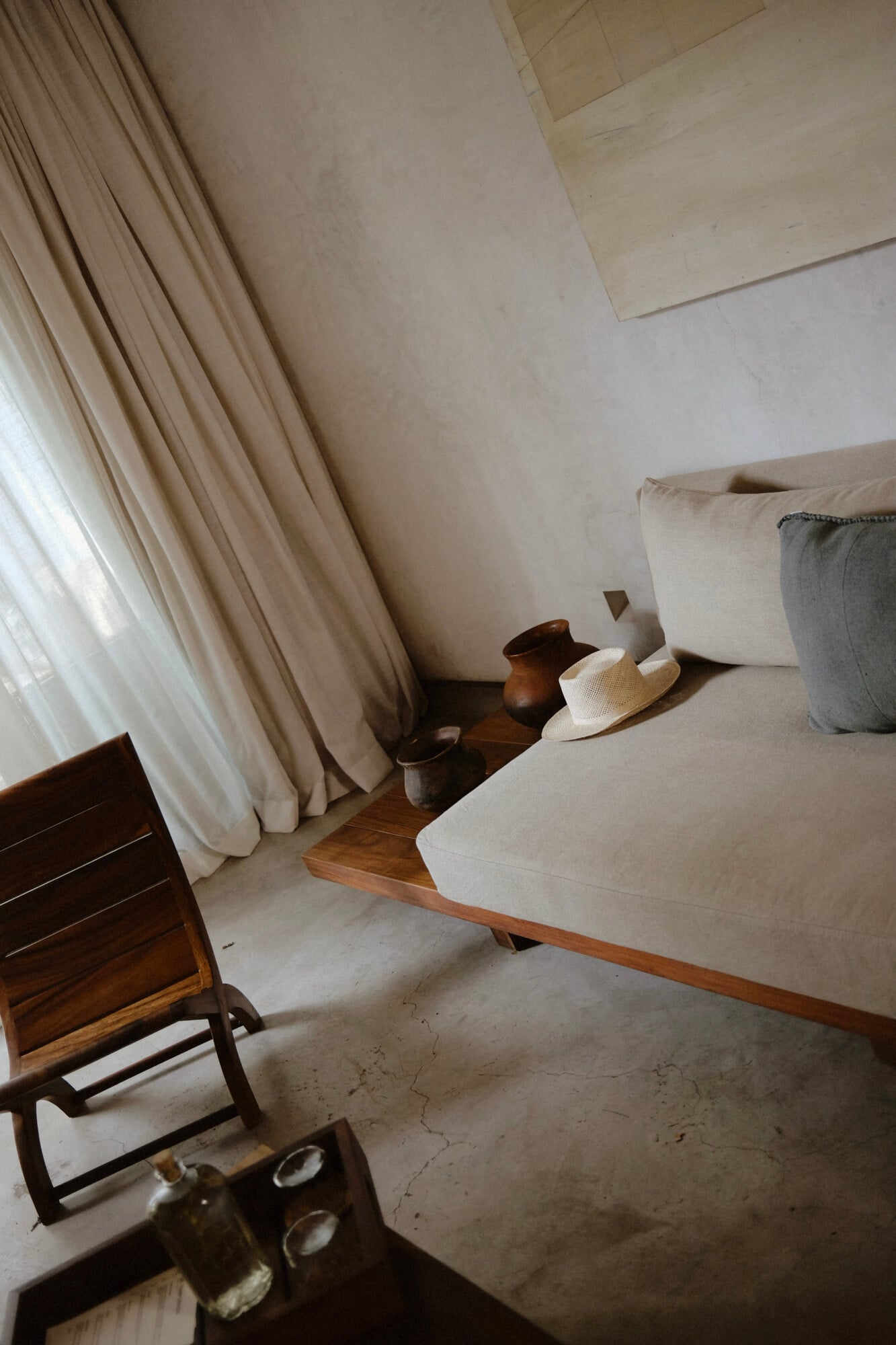 Casa Criollo, Mexico — Minimalist bedroom with cream linen sofa, wooden furniture, natural light through sheer curtains, terracotta pottery, polished concrete floors.