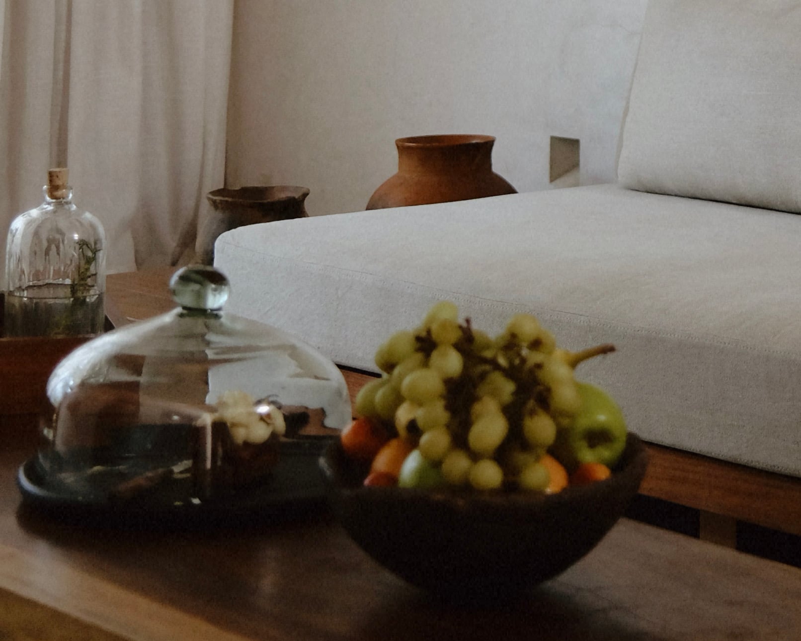 Casa Criollo, Mexico — Minimalist bedroom detail with white linen sofa, ceramic vessels, and fresh grapes in dark bowl on wooden table, neutral palette.