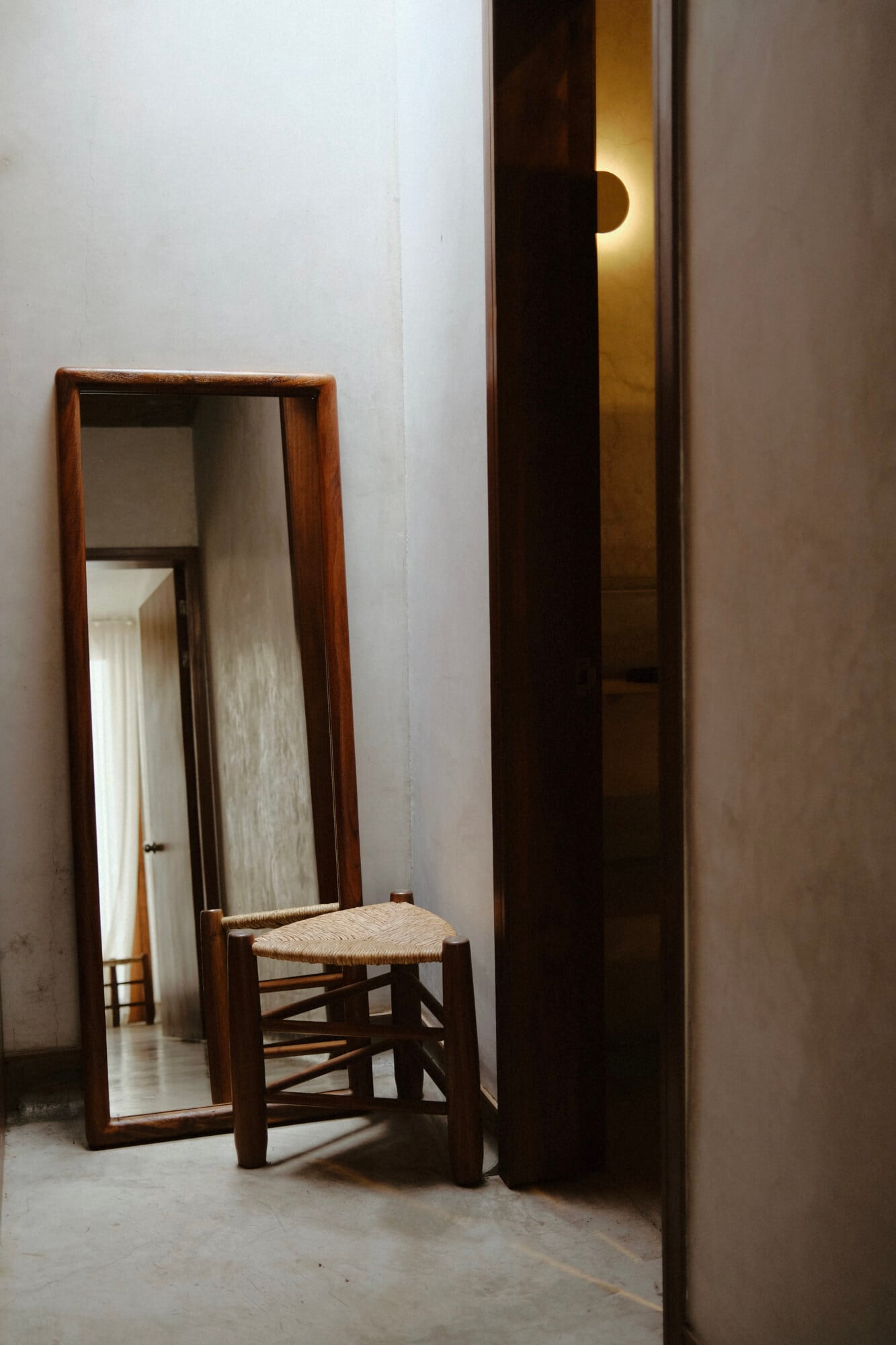 Casa Criollo, Mexico — Minimalist hallway with wooden mirror, rush-seat chair, and warm light filtering through open doorway.