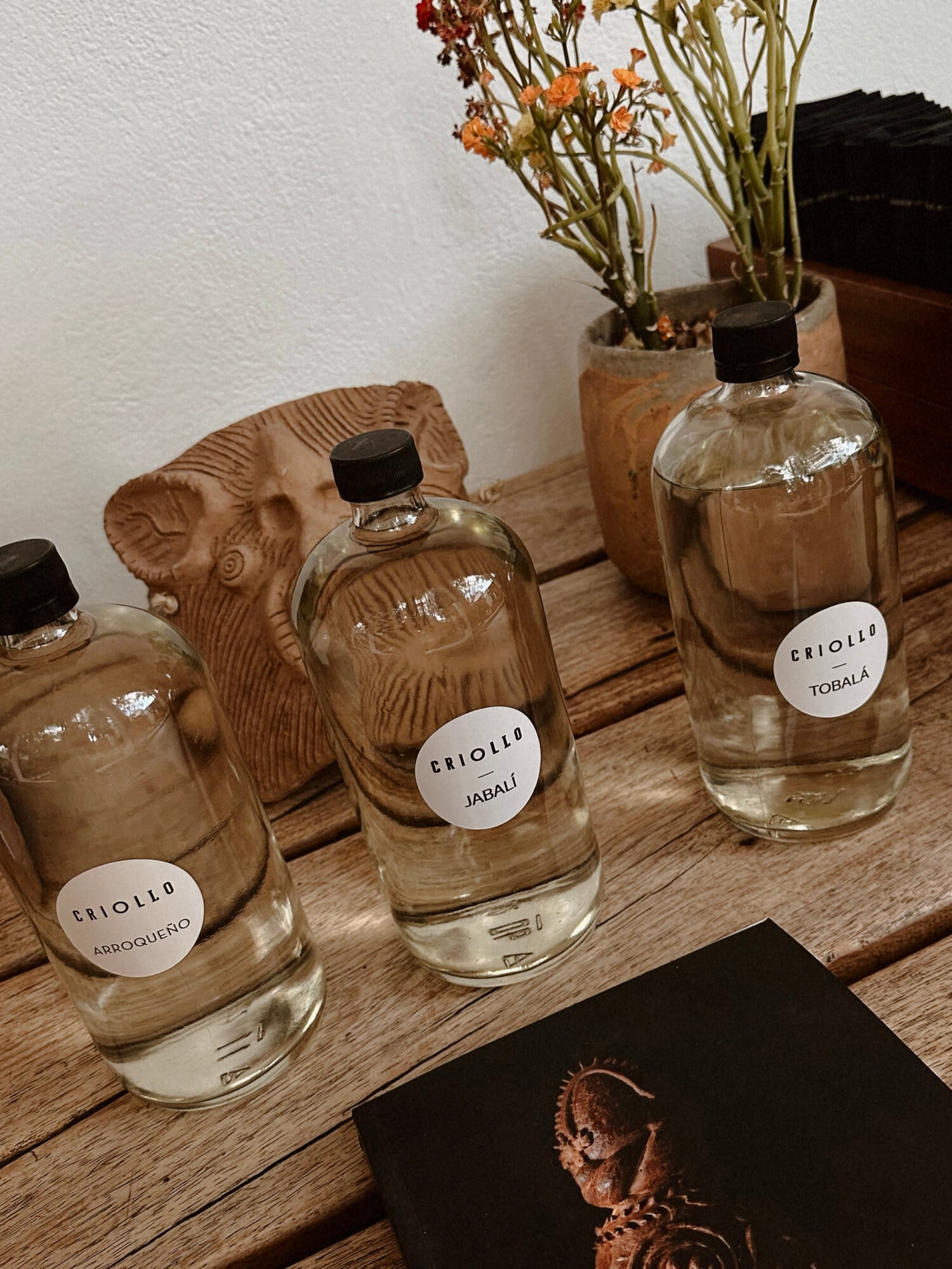Casa Criollo, Mexico — Criollo fragrance bottles with wooden carved sculptures and dried flowers on rustic wood surface, luxury hospitality retail display.