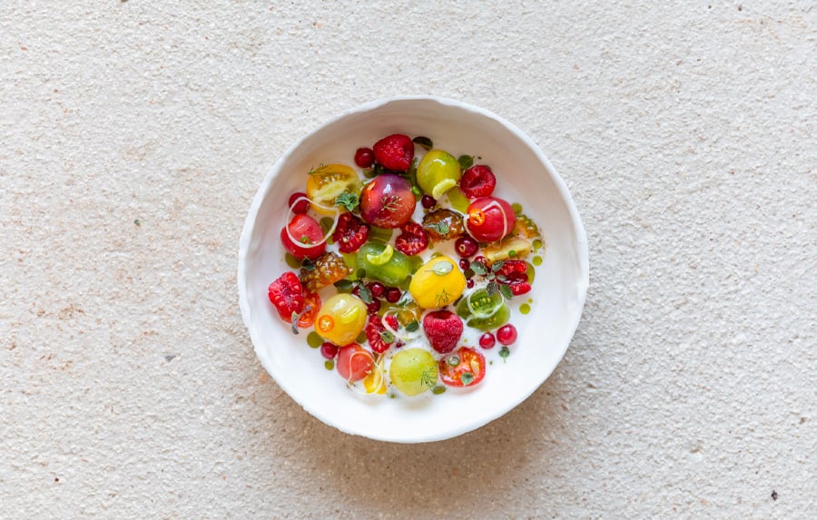 Colorful fresh berries and sliced citrus arranged on white plate for cooking class demonstration, vibrant food styling for luxury hospitality experience.