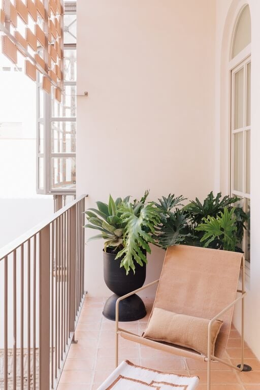 Plácido y Grata, Europe — Minimalist balcony with terracotta flooring, potted plants, canvas chair, white walls, and soft natural light through arched window.