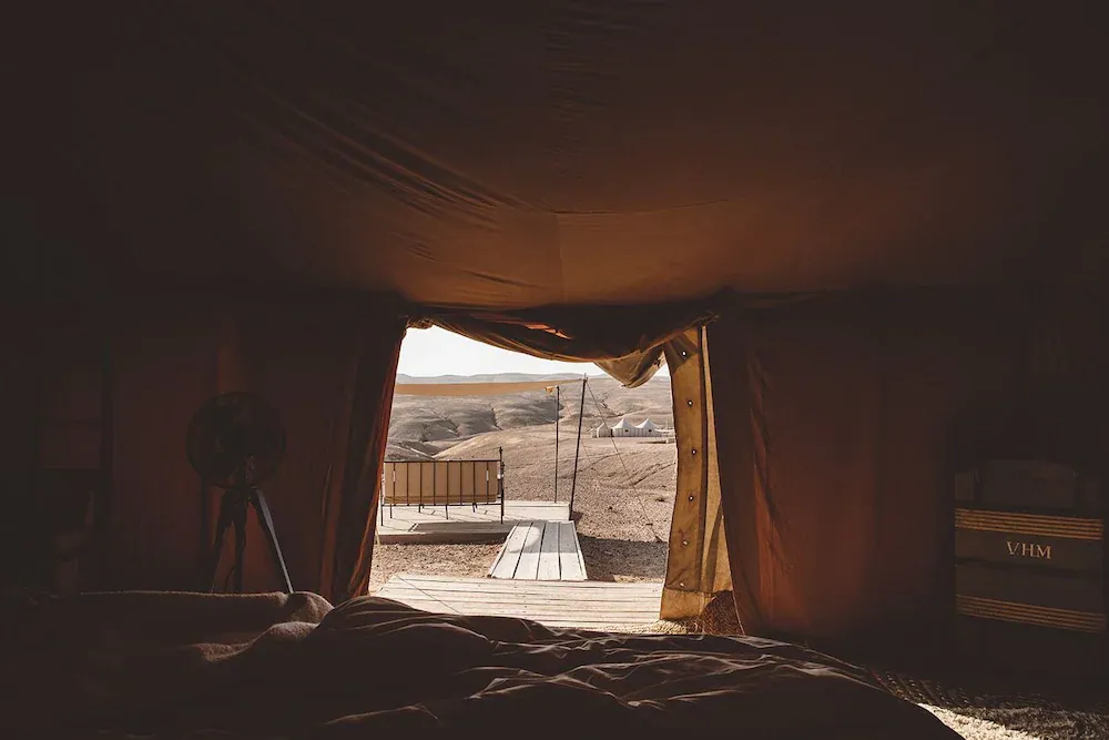 Scarabeo Camp, Africa — Warm canvas tent interior with wooden deck opening to arid desert landscape, golden light filtering through fabric walls.