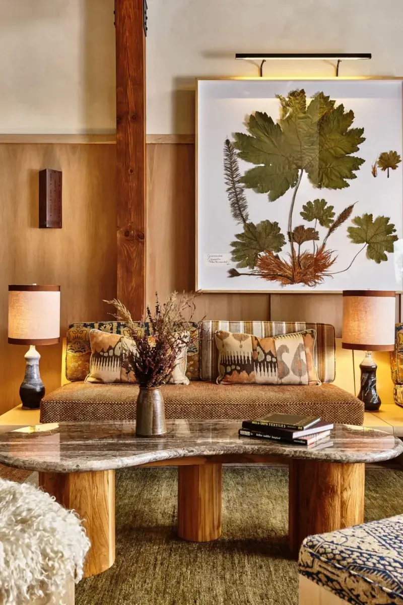 Wildflower Farms, North America — Warm wood-paneled lounge with botanical pressed-flower artwork, curved marble table, linen sofa, and layered lighting creating earthy, sophisticated ambiance.