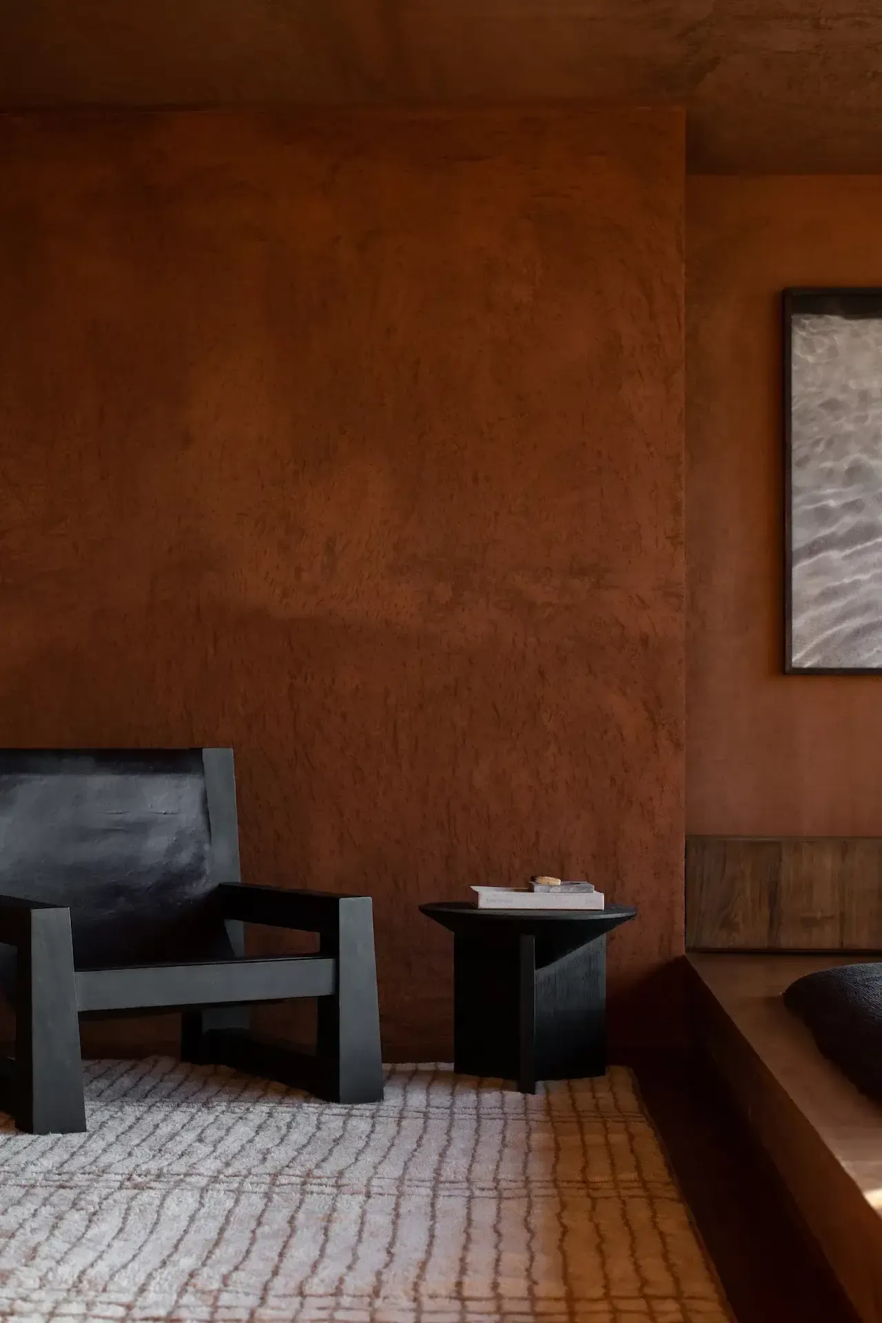 Further Hotel, Asia — Minimalist hotel room with terracotta textured walls, black furniture, geometric patterned rug, and framed artwork creating serene modernist interior design.