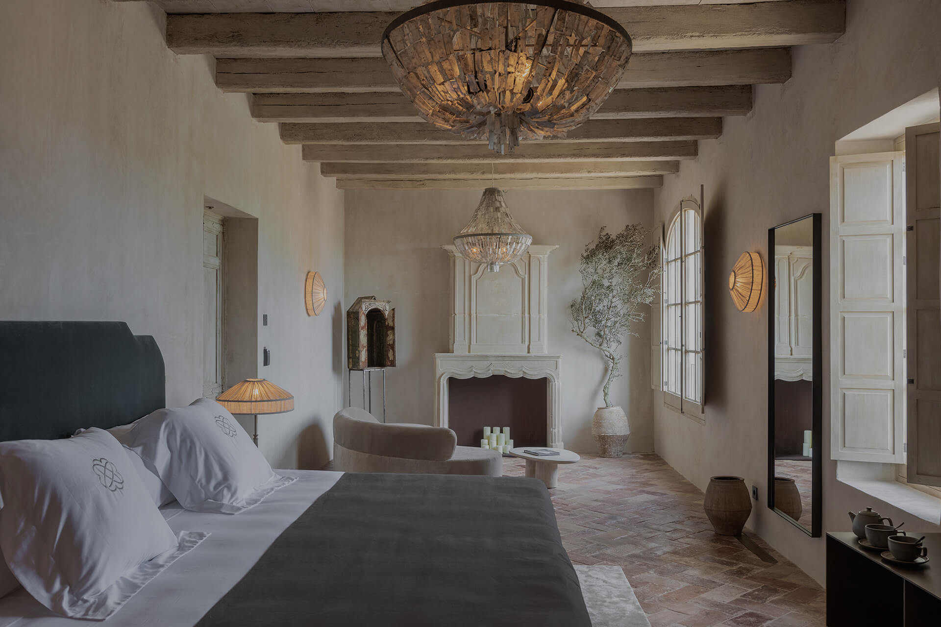 Son Vell, Balearic Islands — Spacious bedroom with exposed wooden beams, fireplace, layered lighting, and Mediterranean terracotta floors blending rustic elegance with contemporary design.