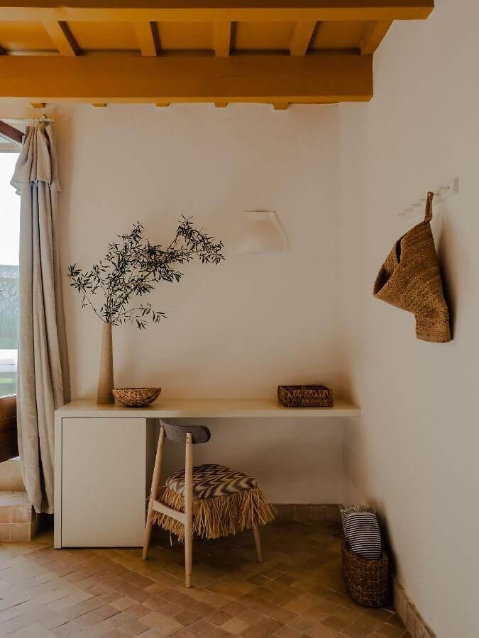 Amagatay, Balearic Islands — Minimalist workspace with woven accents, wooden beam ceiling, natural light, and earthy neutral palette.