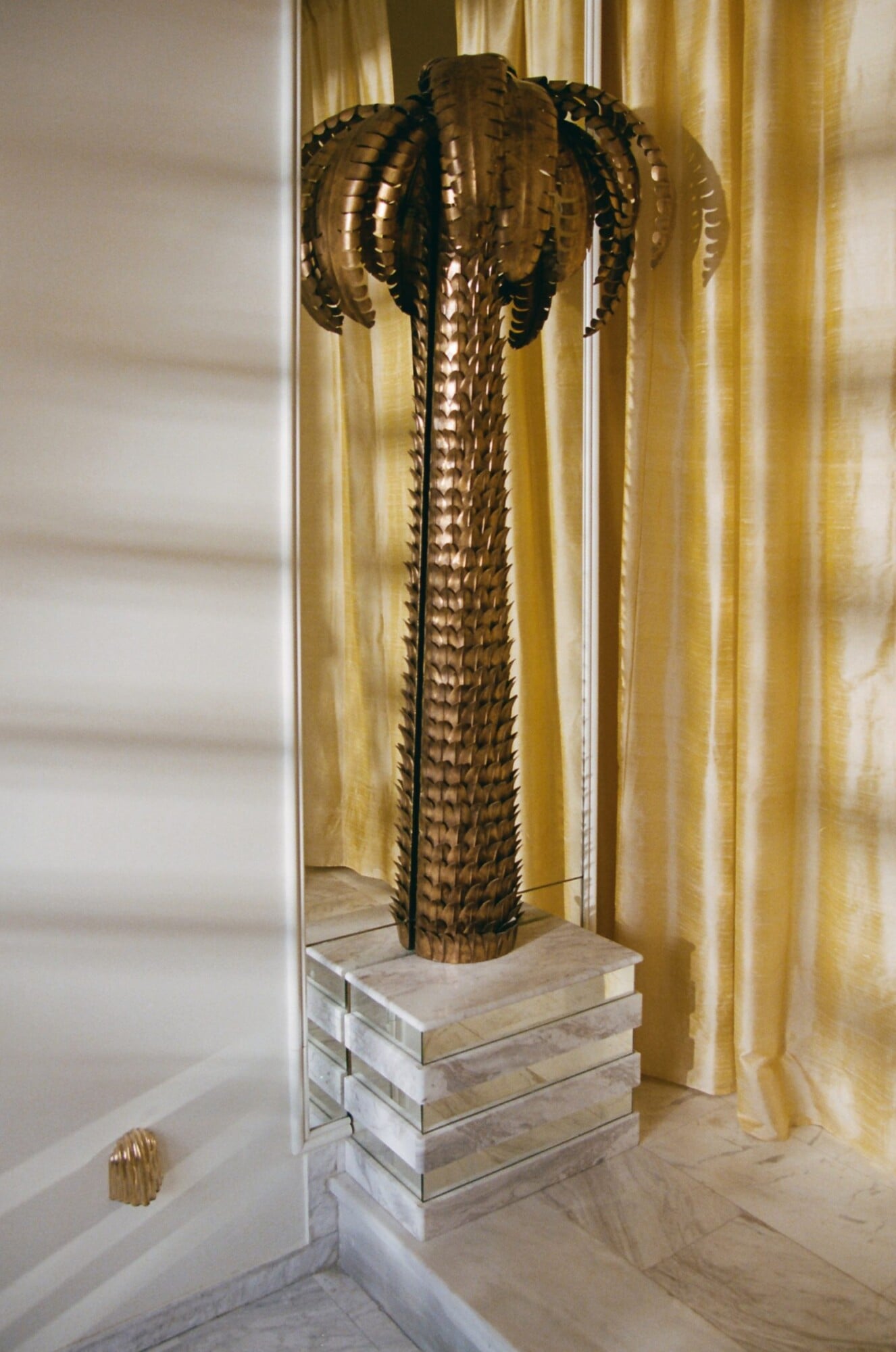Apollo Palm, Europe — Bronze palm sculpture with geometric fronds on travertine plinth, golden curtains and marble flooring in minimalist luxury interior.