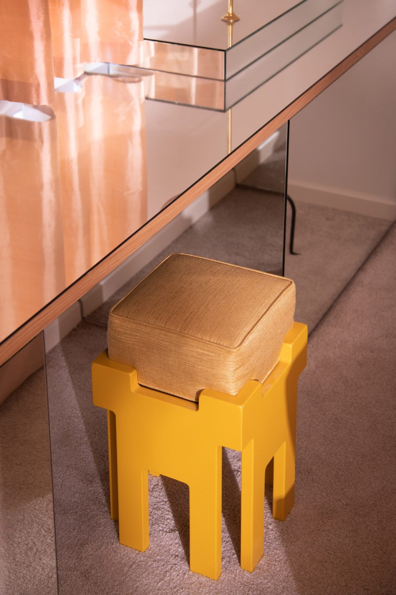 Apollo Palm, Europe — Mustard yellow sculptural stool with woven seat beneath glass partition in minimalist hallway with warm lighting.