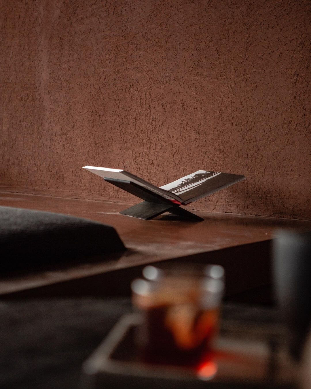 Further Hotel, Asia — Open notebook with pen on wooden desk against textured terracotta wall, warm ambient light casting shadows, minimalist hospitality interior design detail.