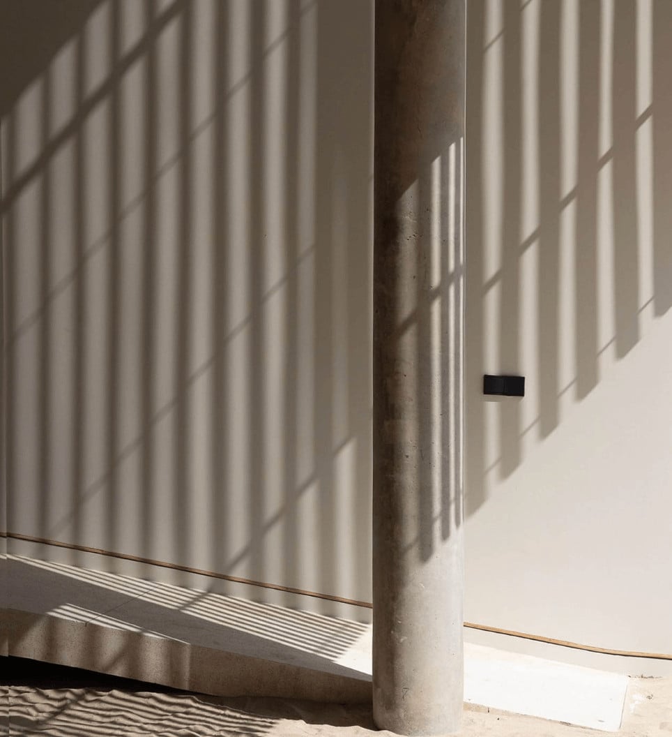 Innit Lombok, Asia — Minimalist concrete corridor with venetian blind shadows, warm natural light, and copper electrical conduit on neutral walls.
