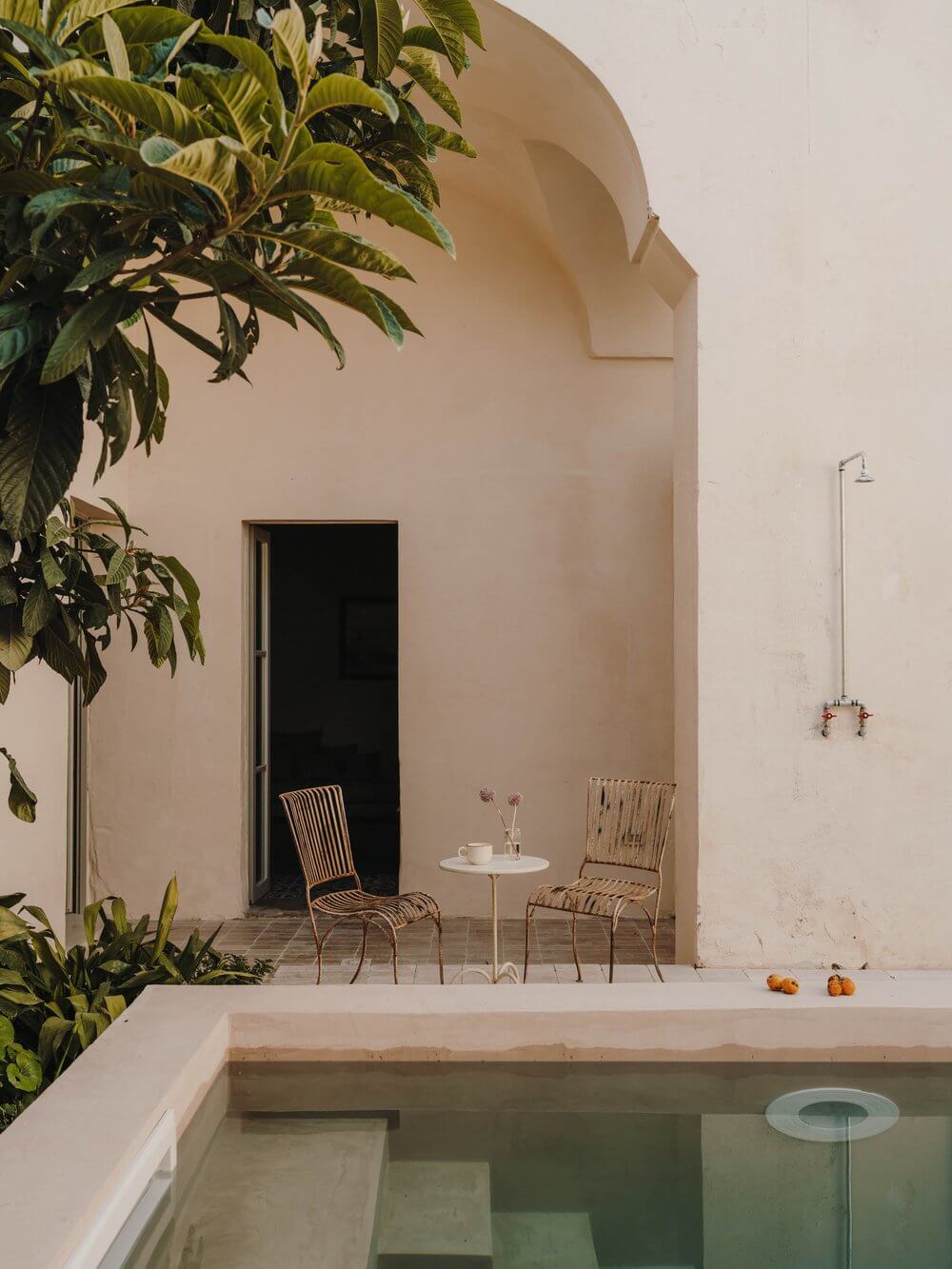 Casa Soleto, Europe — Minimalist courtyard with travertine pool, woven chairs, arched stucco walls, and cascading greenery under Mediterranean light.