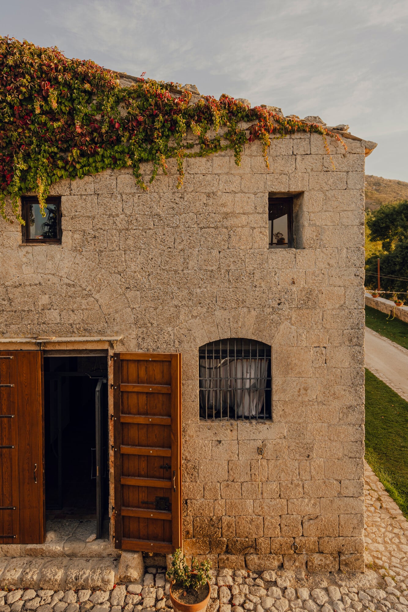 Susafa, Italy — Stone-built rural villa with ivy-draped roof, wooden doors, barred windows, warm afternoon light, Mediterranean countryside aesthetic.