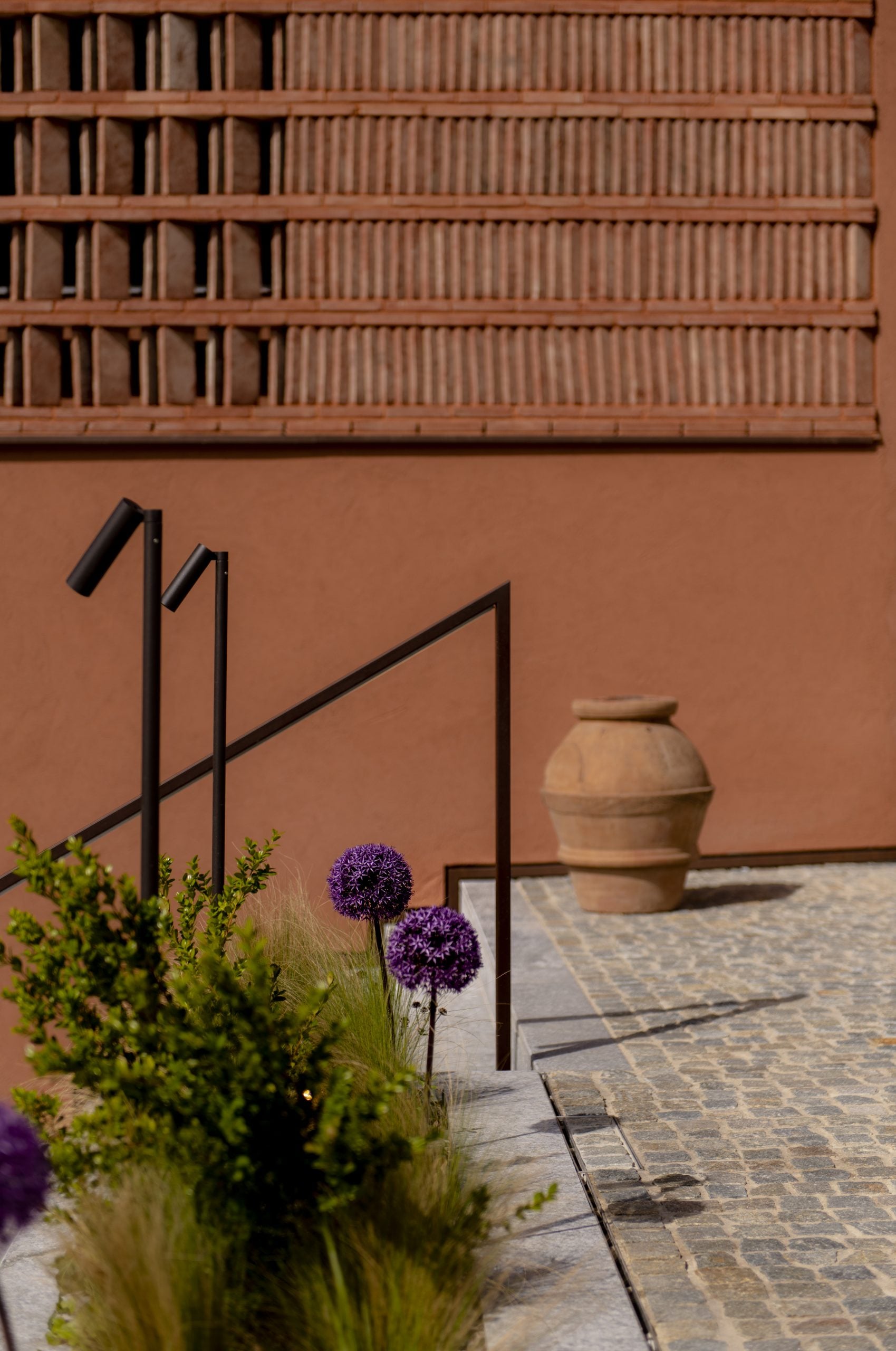 Casa di Langa, Europe — Terracotta courtyard with purple allium flowers, black metal railings, ceramic urn, and minimalist architectural detailing.