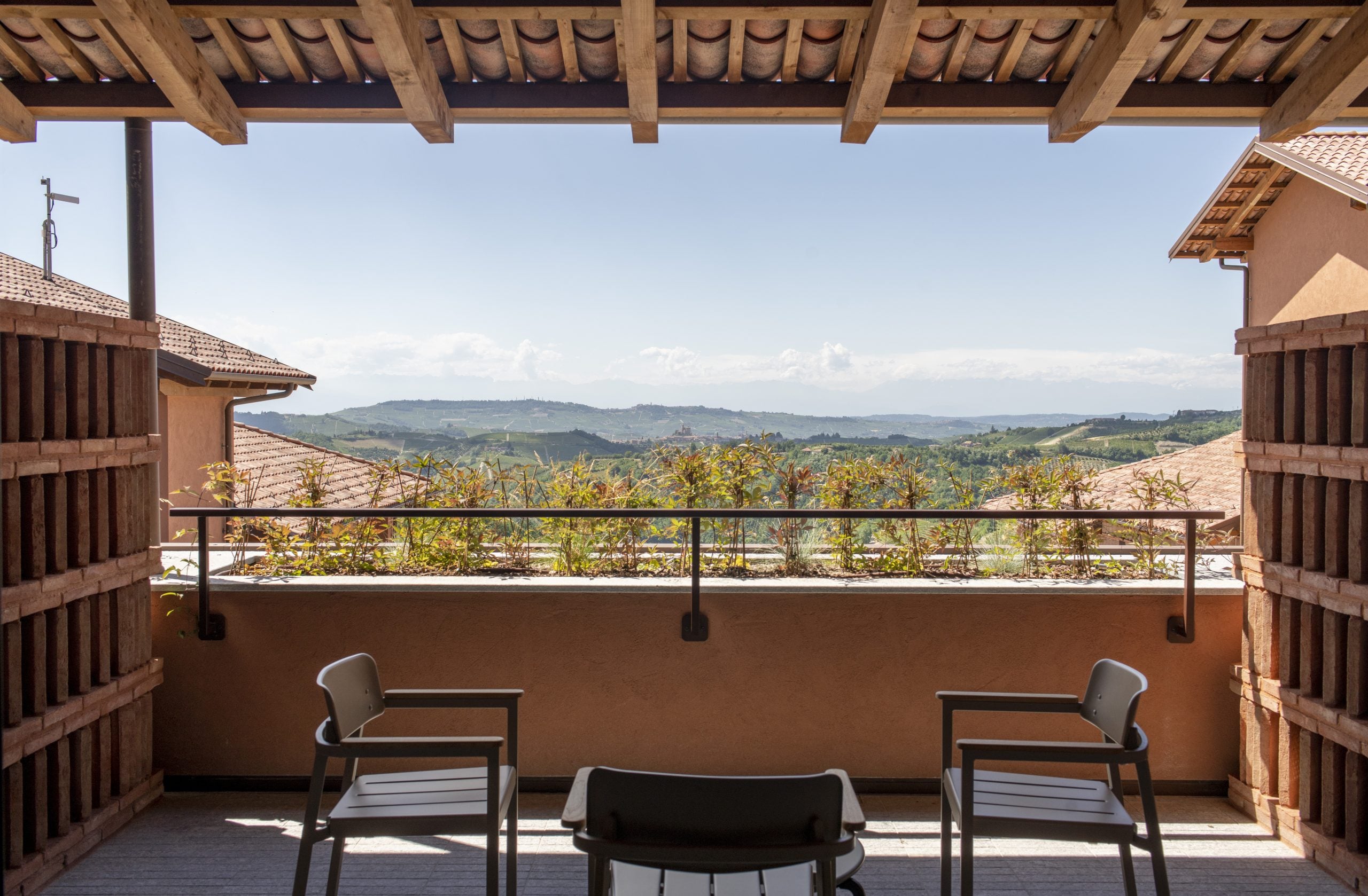 Casa di Langa, Europe — Tuscan terrace with wooden pergola, modern lounge chairs, and rolling countryside views beneath clear sky.