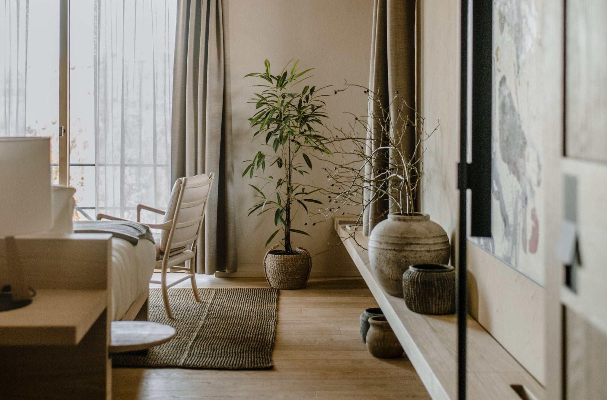 Casa di Langa, Europe — Minimalist hotel room with bamboo plant, woven vessels, linen seating, sheer curtains, and natural light through floor-to-ceiling windows.