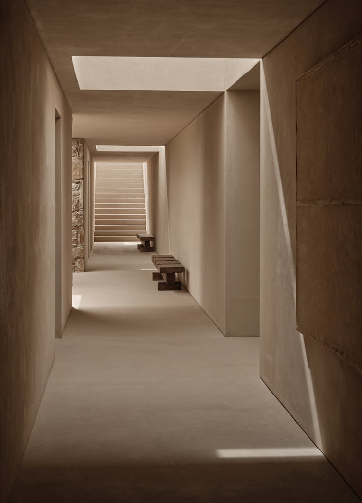 En Kyanó, Europe — Minimalist corridor with skylights, concrete walls, and stepped wooden platforms leading to bright louvered windows, architectural gallery space.
