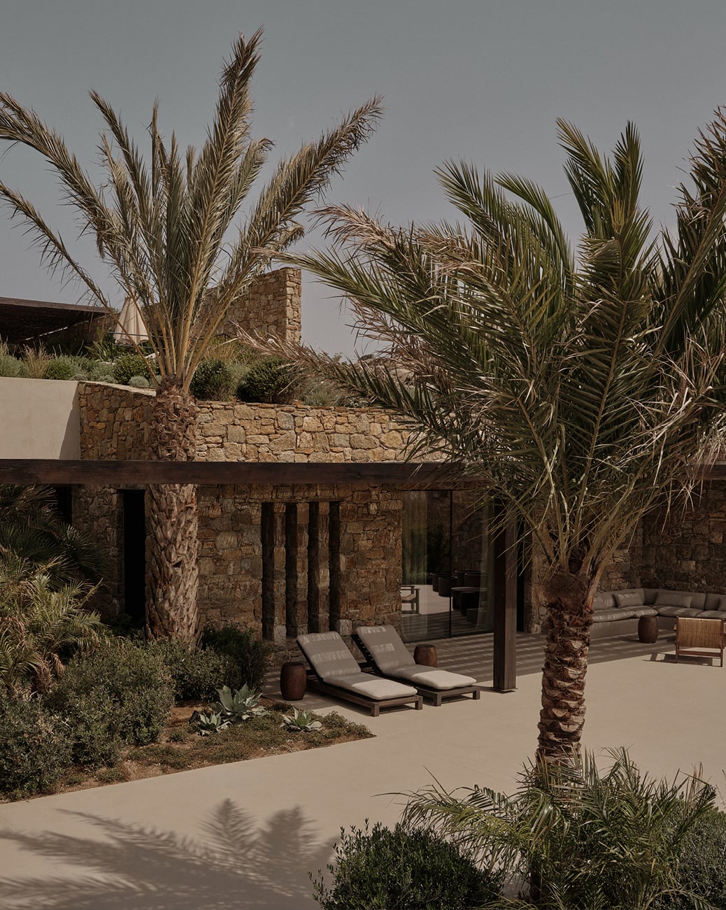 En Kyanó, Europe — Stone villa with palm trees, wooden pergola, loungers, and minimalist courtyard in warm Mediterranean light.