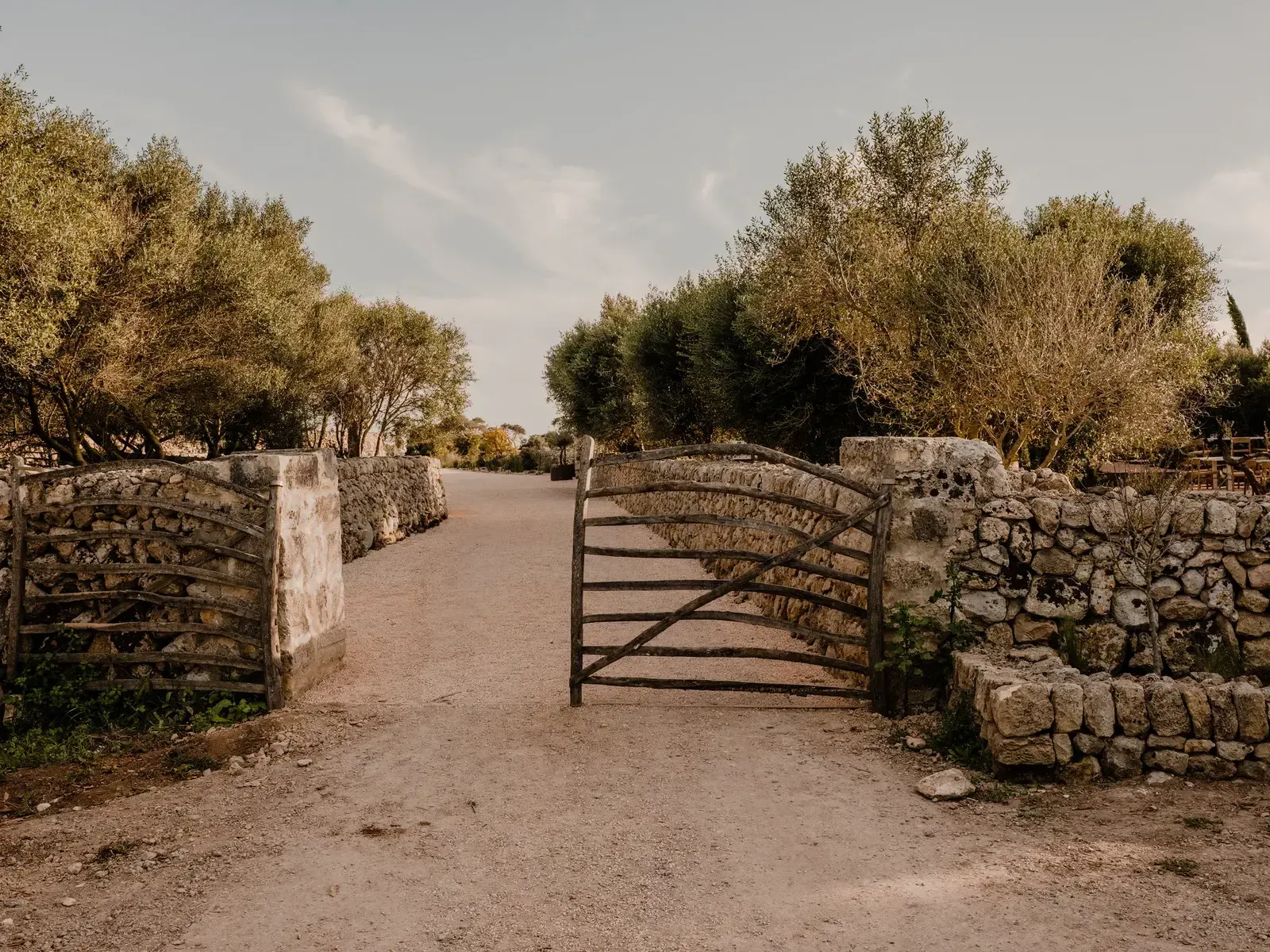 Amagatay, Balearic Islands, Spain — Weathered wooden gate and stone walls framing tree-lined dirt pathway in Mediterranean countryside estate.
