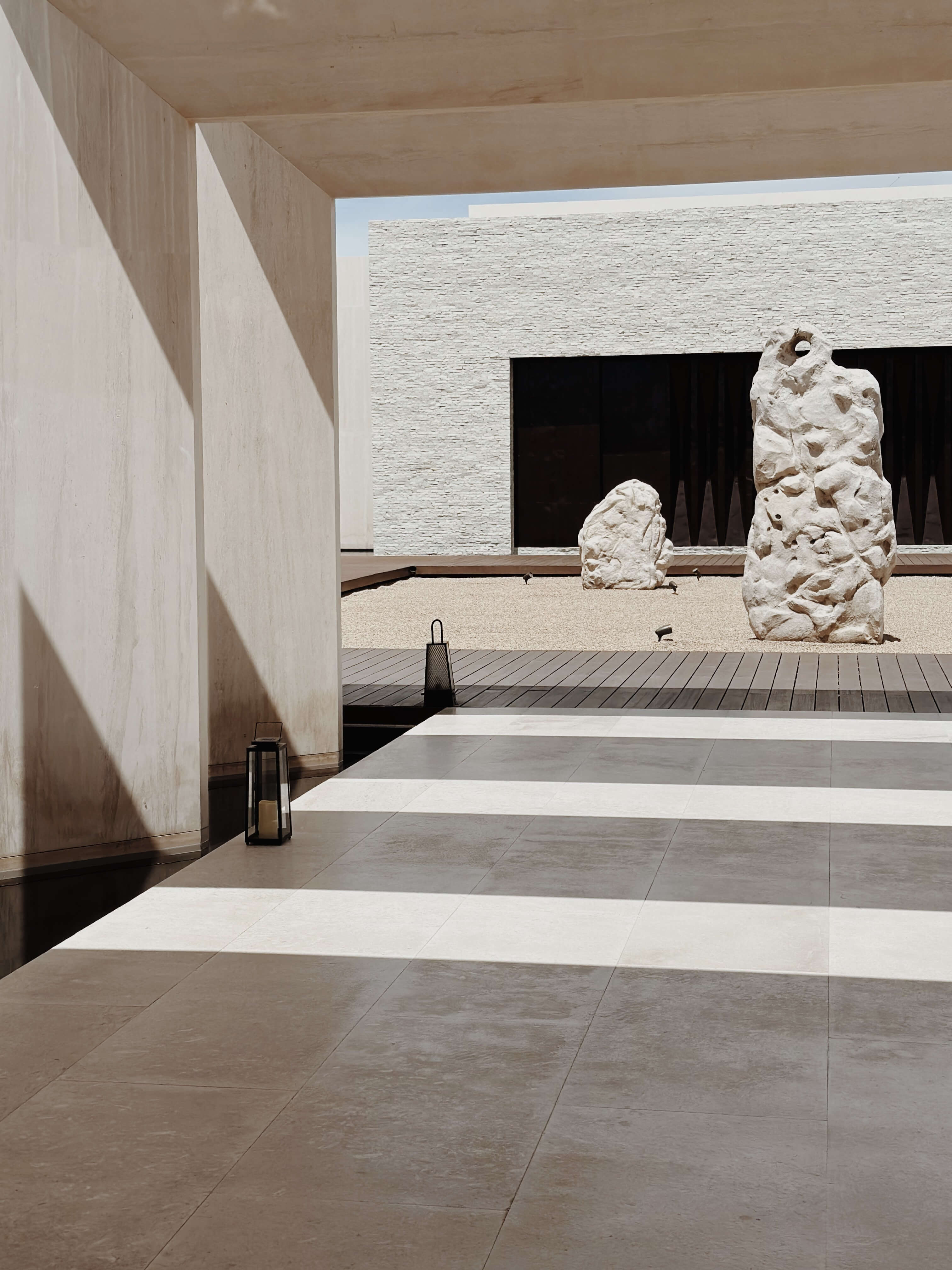 Nobu Los Cabos, Mexico — Minimalist courtyard with concrete pavilion, sculptural white stone elements, and striped wooden deck overlooking desert landscape.