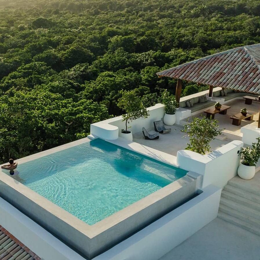 Hotel Esencia, Mexico — Infinity pool with turquoise water overlooking dense jungle canopy, white terrazzo deck, teak pergola, minimalist tropical architecture.
