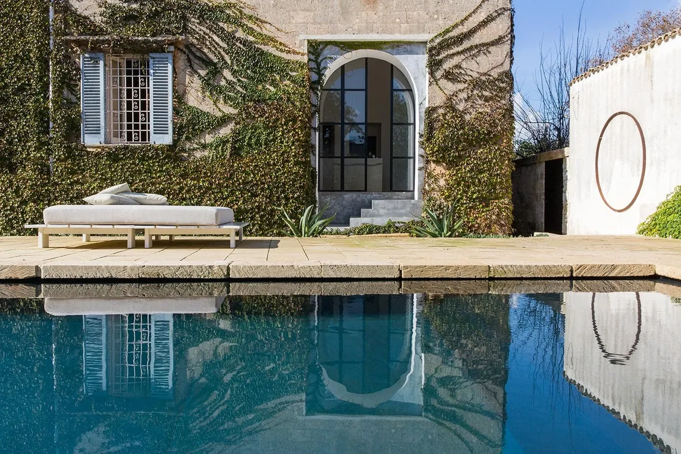 Palazzo Daniele, Europe — Ivy-covered limestone facade with arched doorway reflected in still pool, modernist bench, Mediterranean courtyard design.