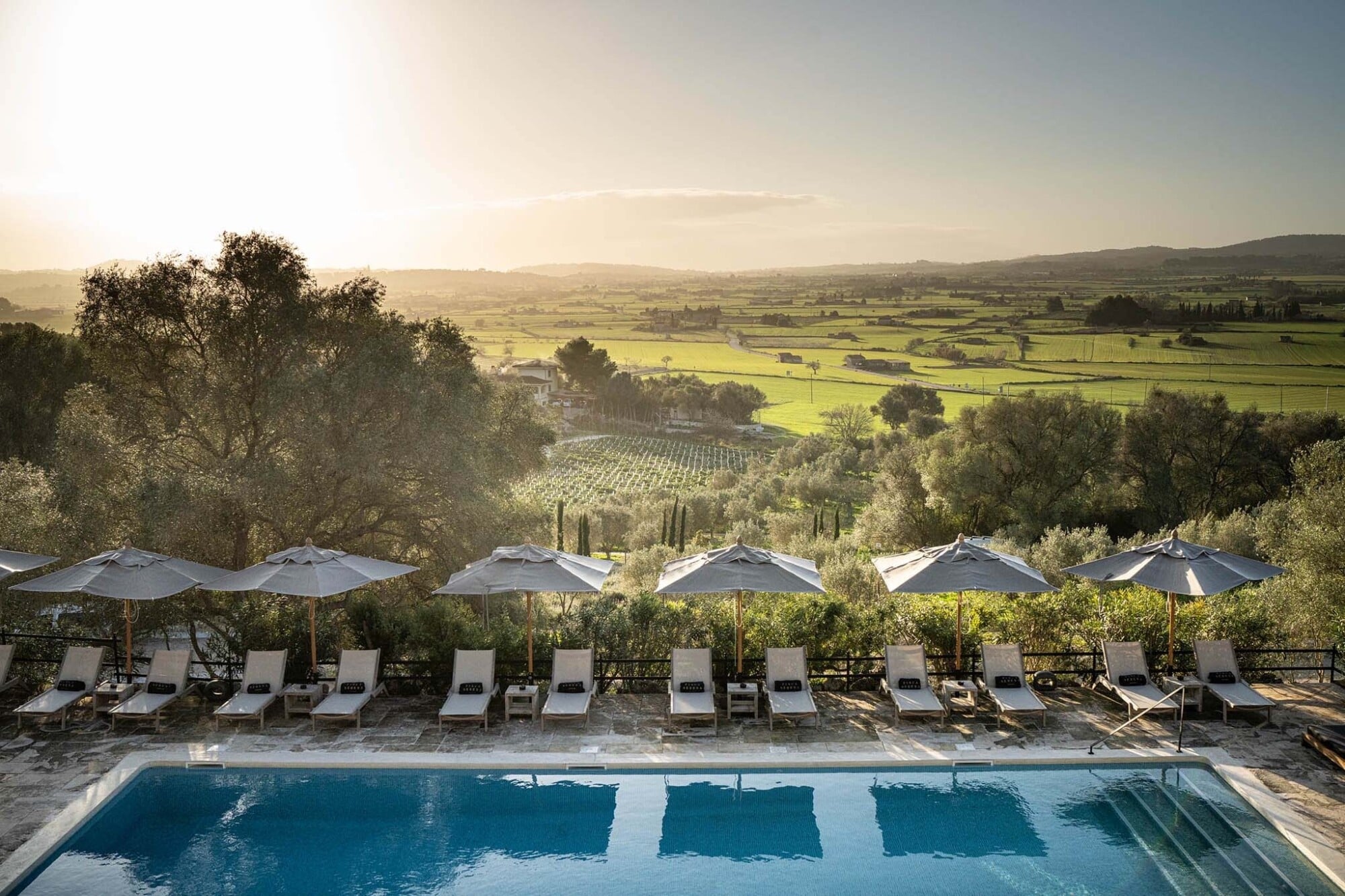 Finca Serena, Balearic Islands, Spain — Infinity pool with loungers and umbrellas overlooking olive groves and Tuscan-style countryside at golden hour.
