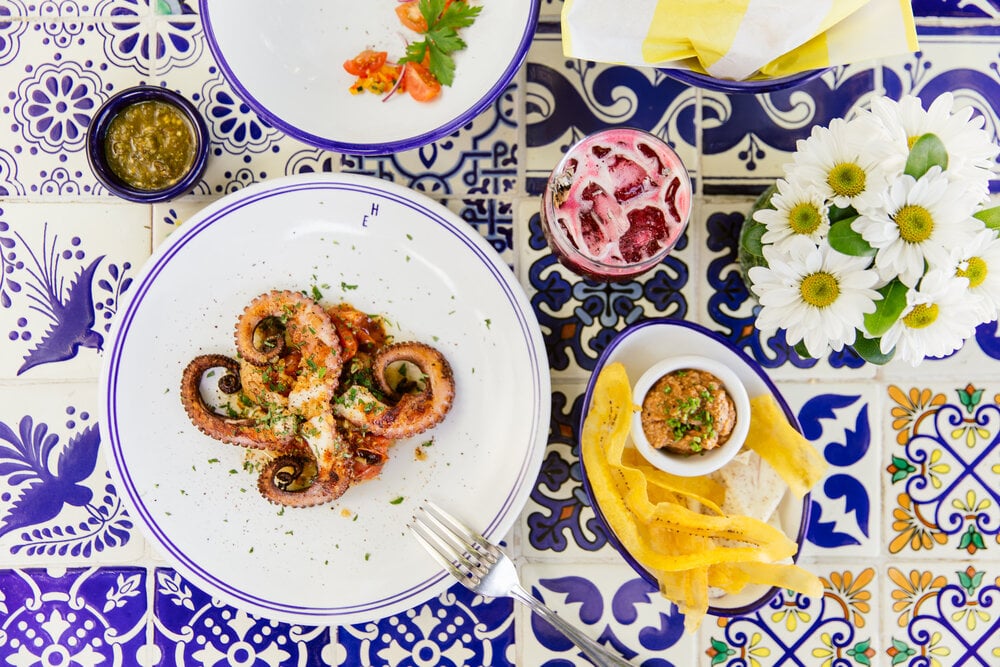 Hotel Esencia, Mexico — Grilled octopus with garlic and herbs on blue and white patterned tableware, daisies and condiments arranged on ornamental tiles.