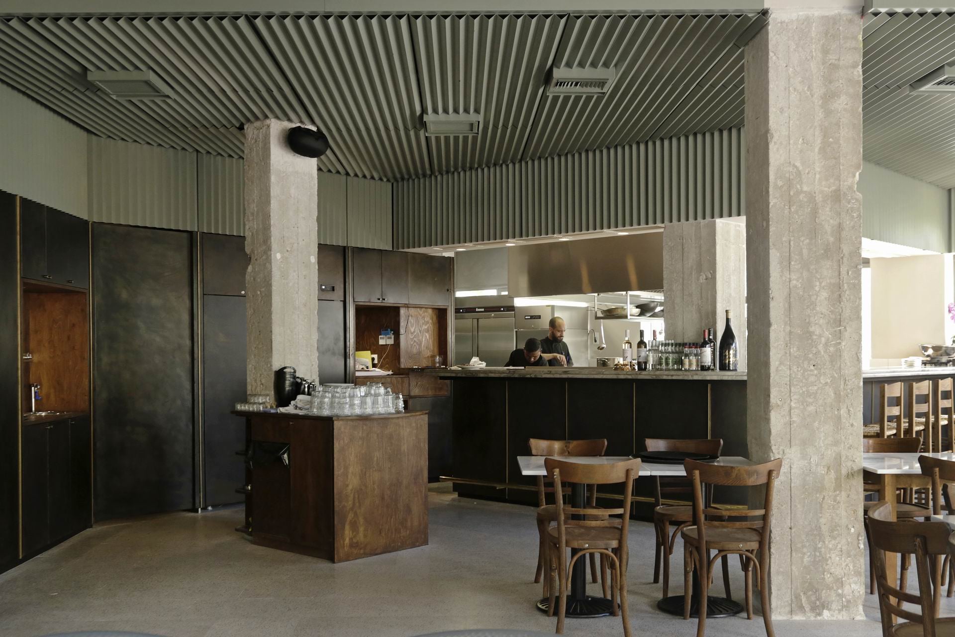 ΦΙΤΑ, Europe — Open kitchen with dark wood counter, concrete columns, corrugated ceiling, and bentwood dining chairs in minimalist industrial bistro setting.