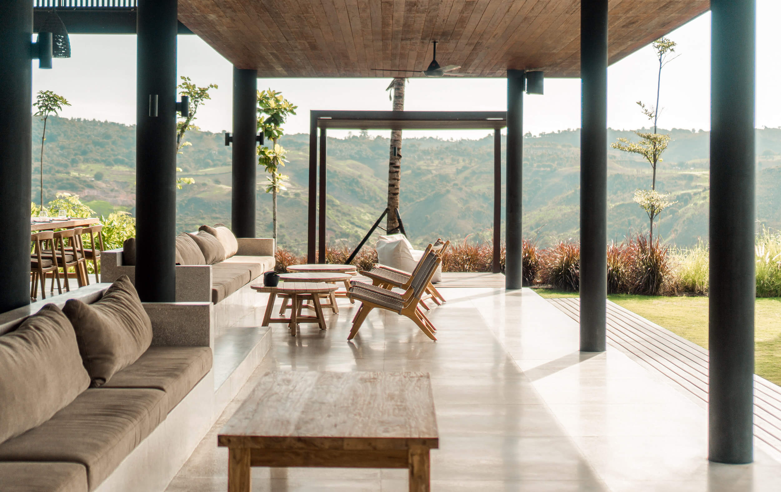 Somewhere Lombok, Bali, Indonesia — Modern pavilion with polished concrete floors, dark columns, and teak furnishings overlooking terraced valley landscape at sunrise.