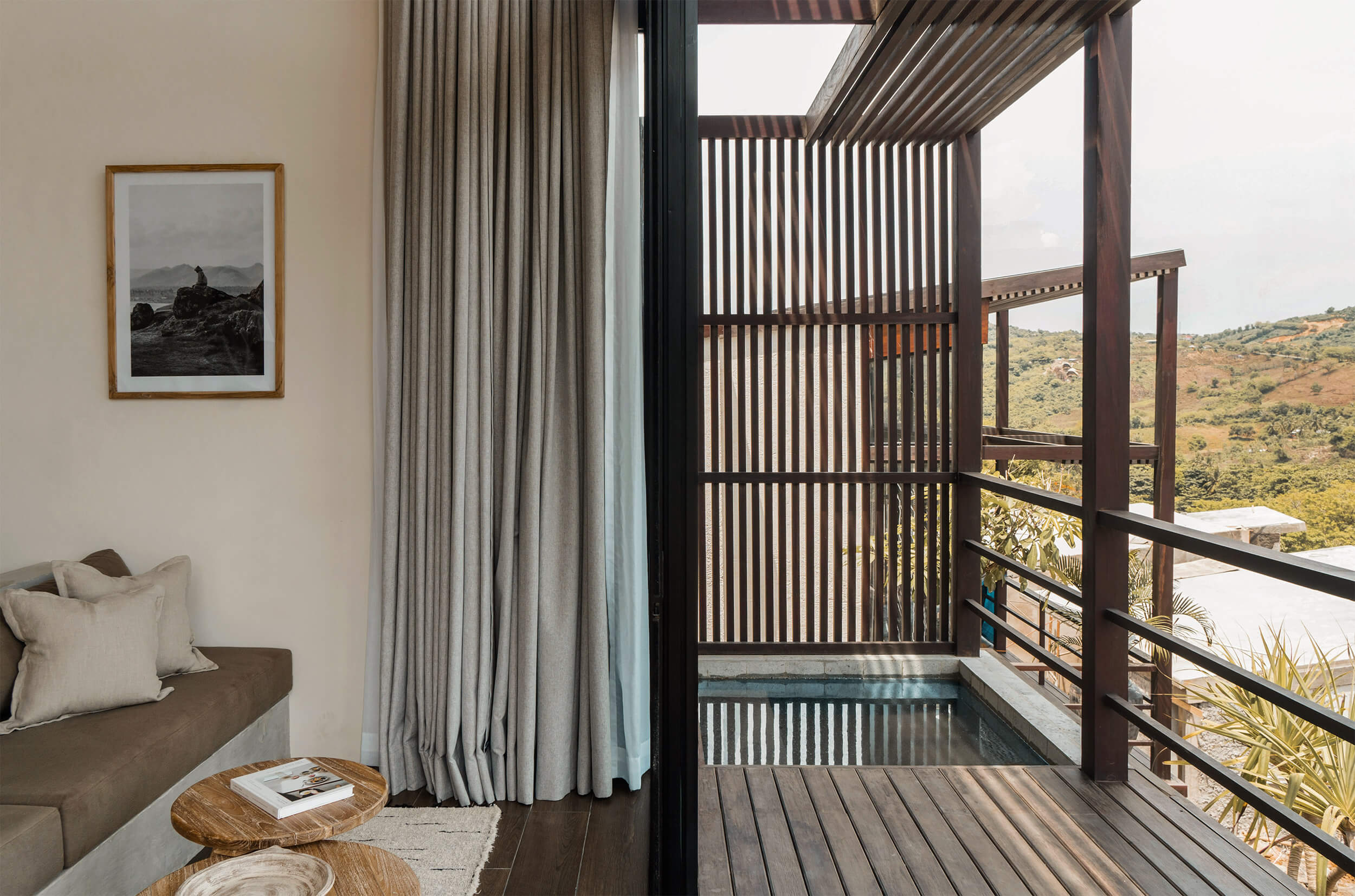 Somewhere Lombok, Indonesia — Modern bedroom with slatted timber screens, linen curtains, and expansive views of rolling hillside landscape through floor-to-ceiling glass doors.