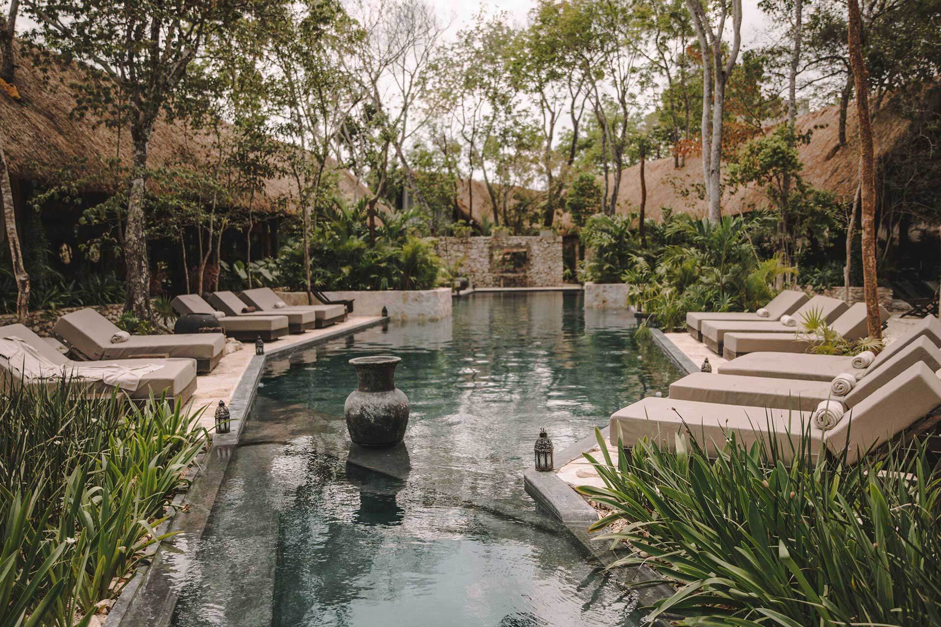 Bardo, Mexico — Limestone pool terrace lined with lounge chairs, cenote-fed waters, jungle canopy, and stone architecture in dappled light.