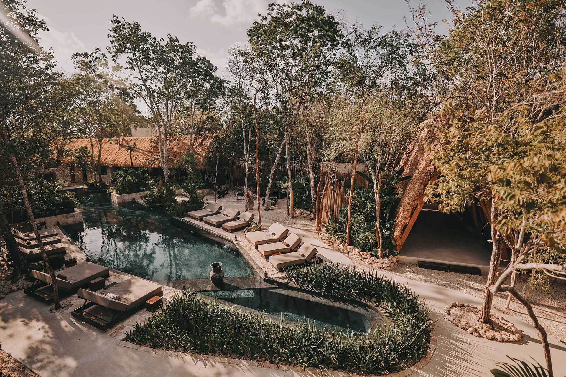 Bardo, Mexico — Turquoise cenote pool with limestone terraces, lounge chairs, and tall trees in tropical forest setting at dusk.