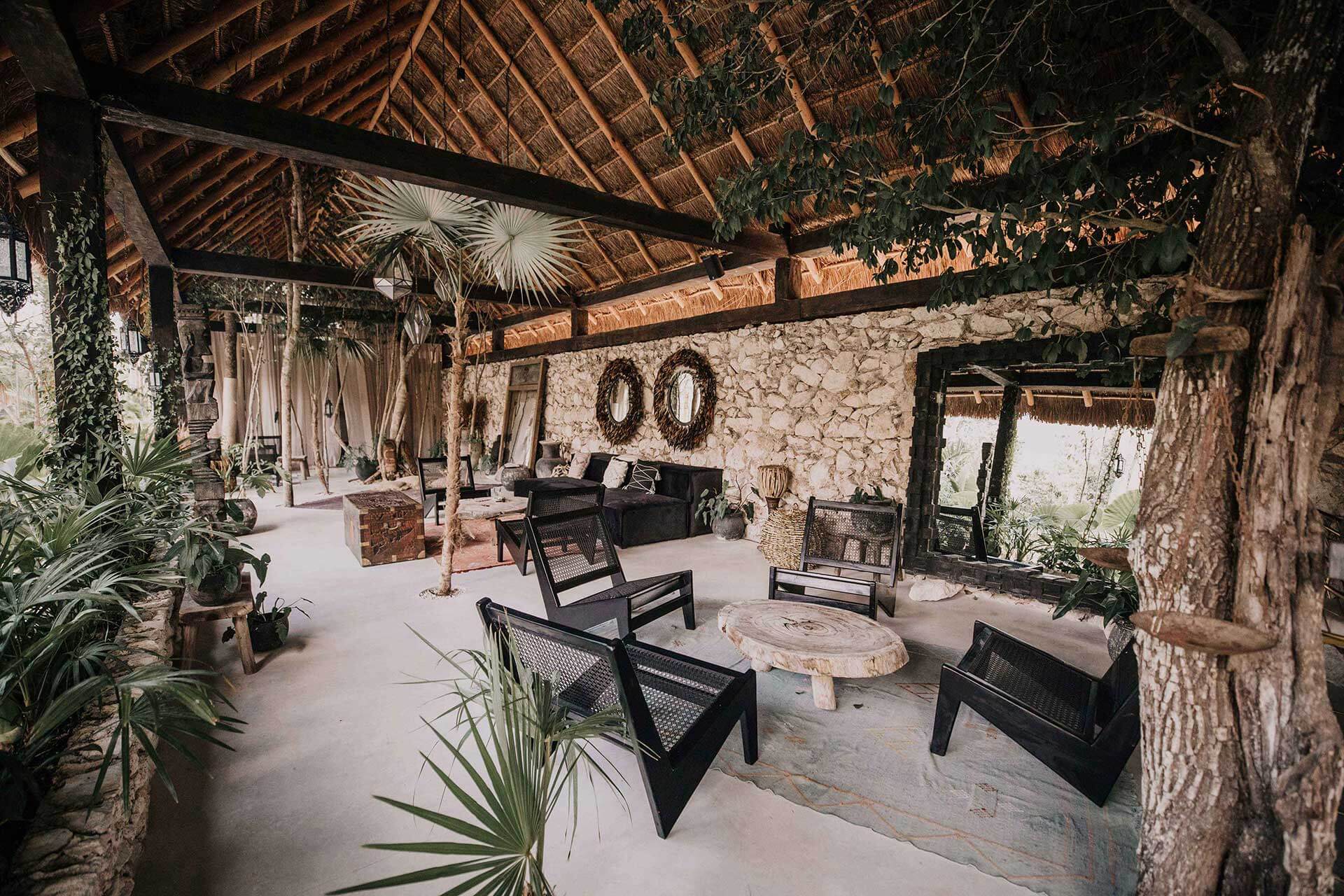 Covered pavilion at Bardo with stone walls, thatch roof, black lounge chairs, and mature trees creating dappled shade.