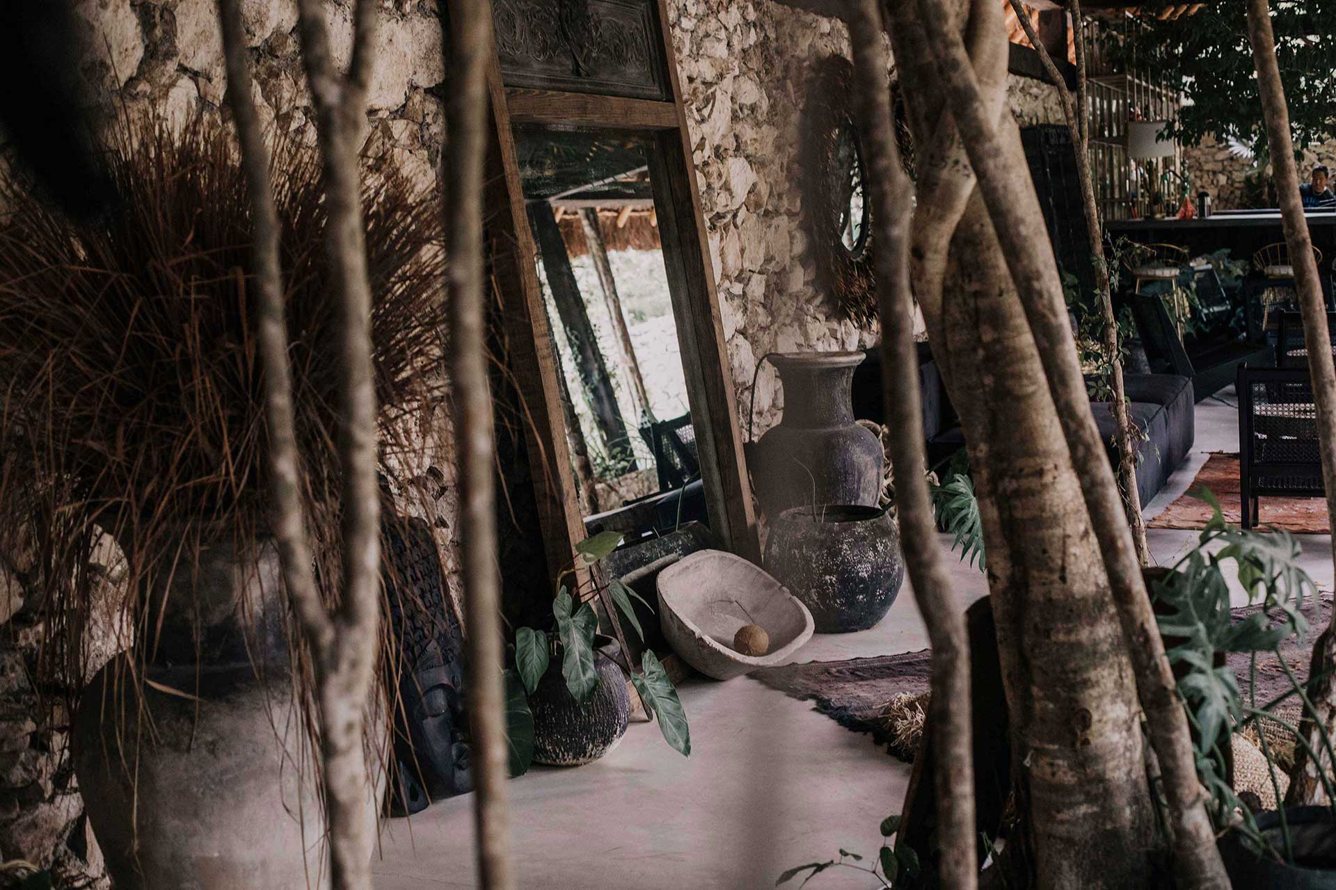 Weathered courtyard detail at Bardo with pale stone walls, dried palm fronds, and terracotta vessels in dappled light.