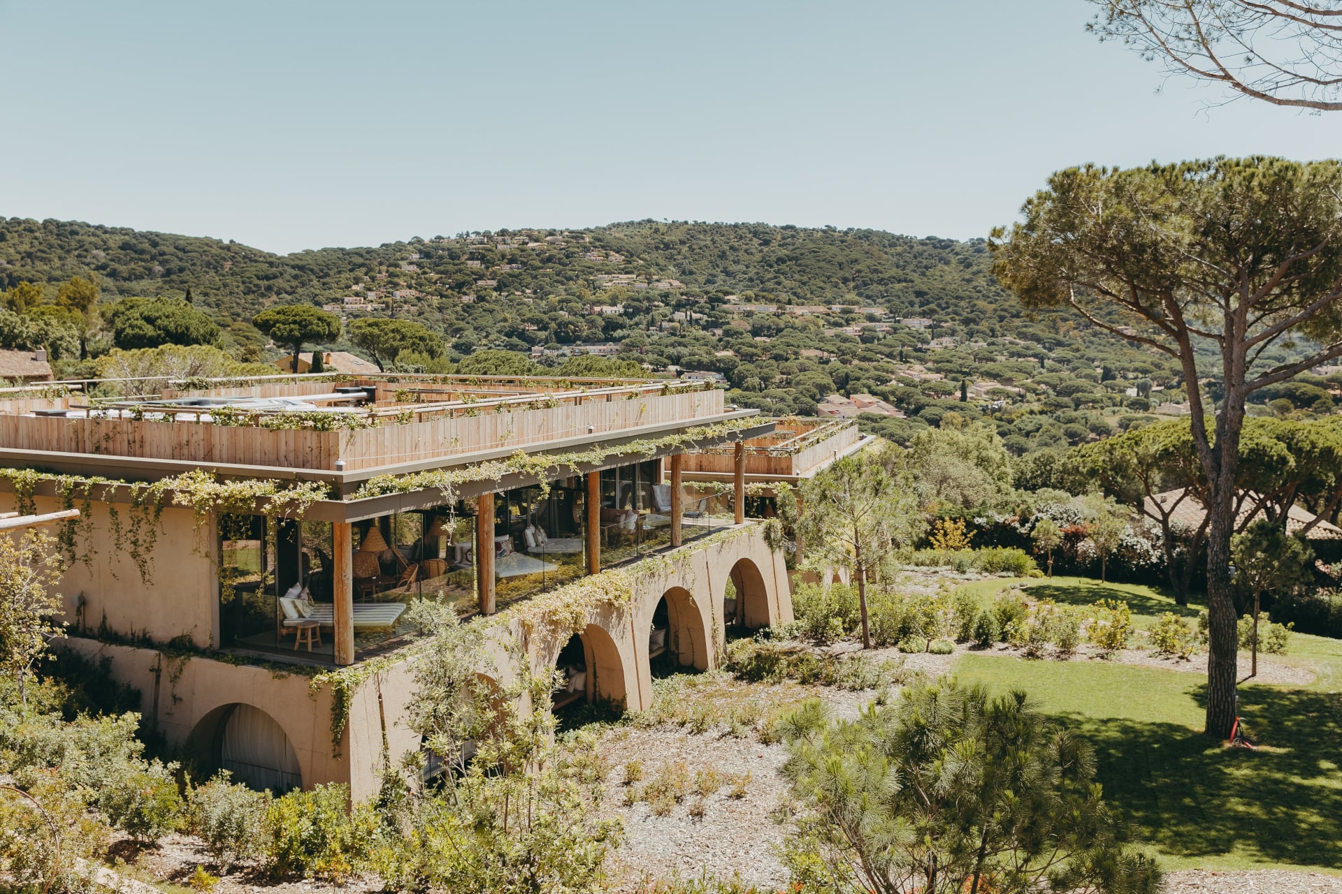 Lily of the Valley, Europe — Terraced stone villa with wooden pergolas and green roofs overlooking forested Mediterranean hills, modernist hospitality architecture.