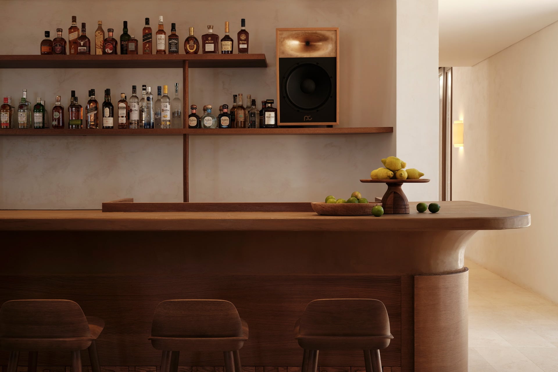 Gundari, Greece — Curved wooden bar with cognac bottles on floating shelves, fresh citrus display, and upholstered seating in minimalist luxury interior.