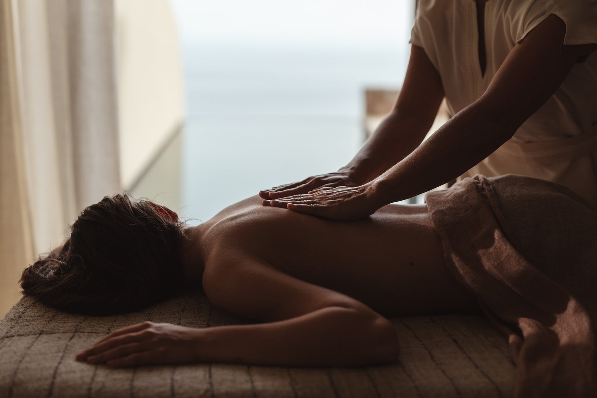 Gundari Spa, Greece — Therapist administering back massage in minimalist spa room with coastal light and linen textures.