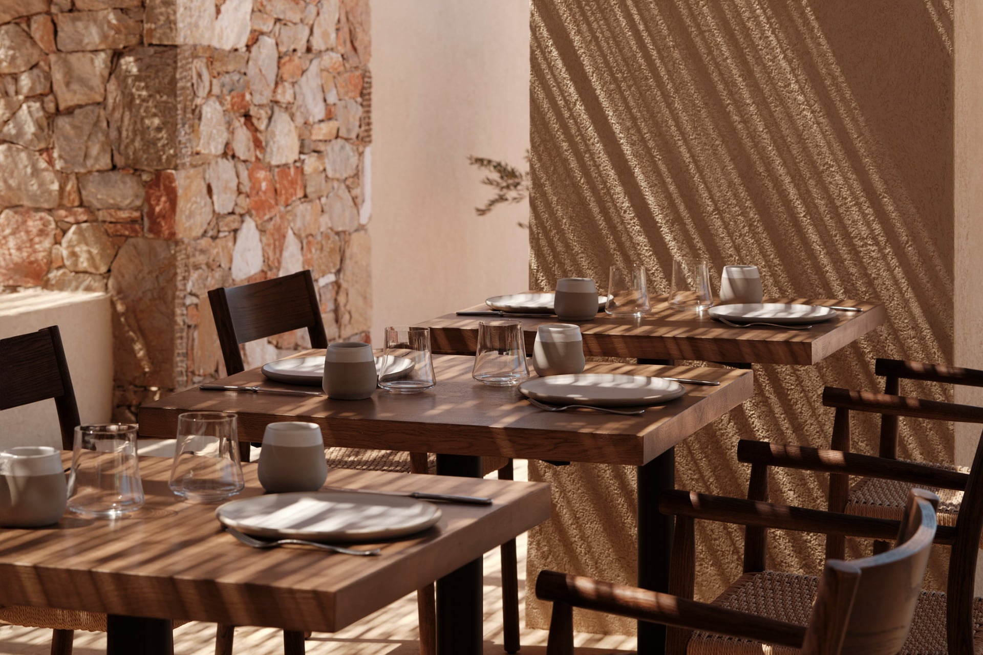 Gundari, Greece — Dining room with wooden tables, stone brick wall, woven textile panels, natural light casting shadow patterns, minimalist tableware and glassware.