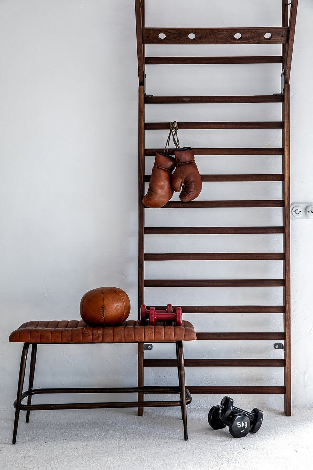 Yoga & Fitness Training, Balearic Islands — vintage wooden wall bars with hung boxing gloves, leather bench, dumbbells, and medicine ball in minimalist studio.