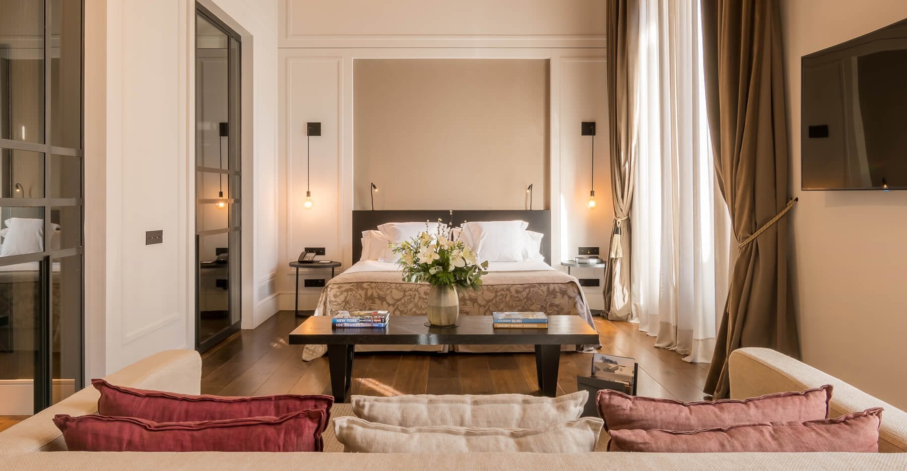 Sant Francesc Hotel Singular, Balearic Islands — Luxury suite with cream walls, dark wood bed, pendant lighting, and contemporary furnishings overlooking spacious living area.
