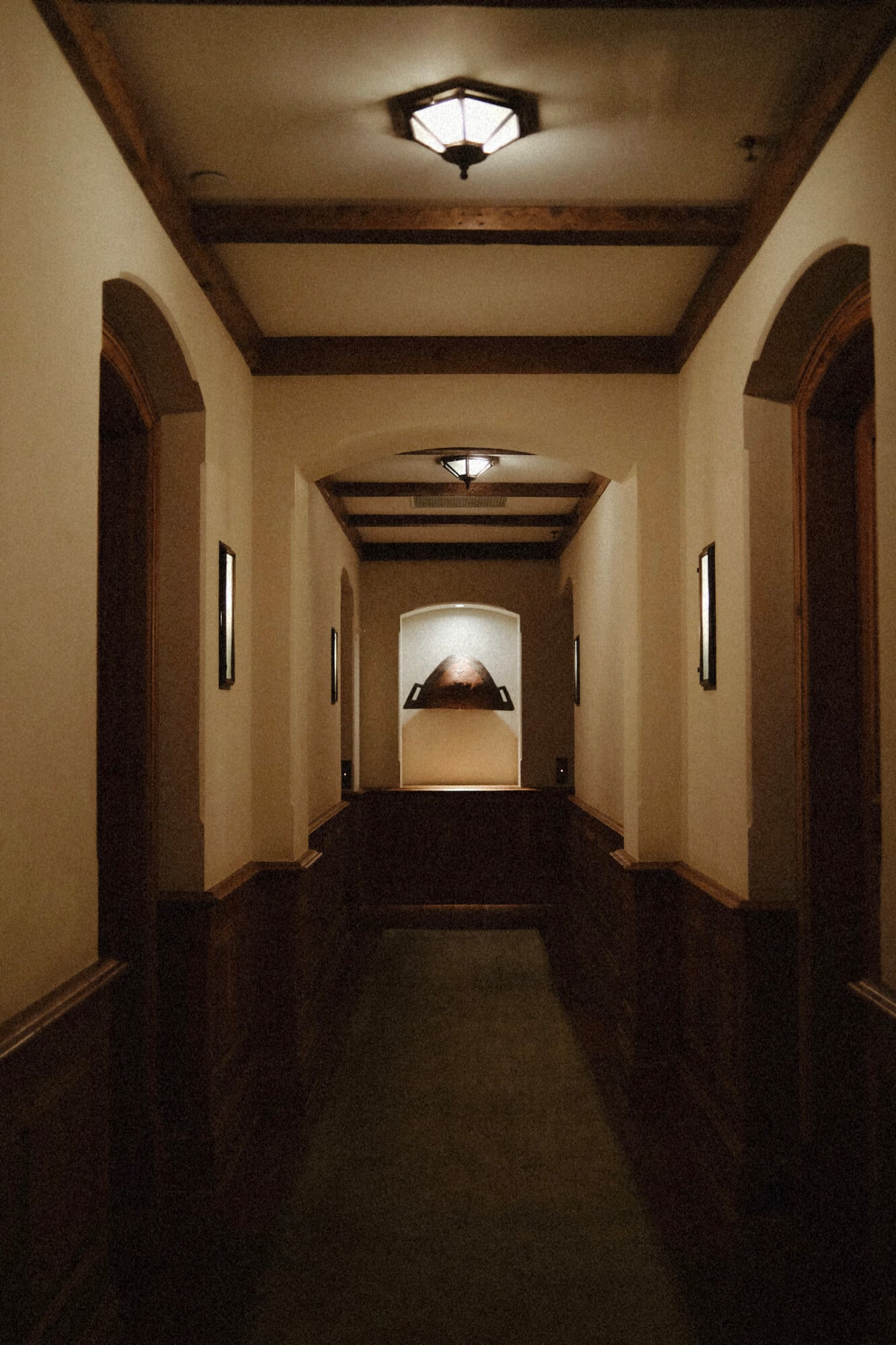 The Greenwich Hotel, North America — Illuminated hallway with exposed beam ceiling, arched doorways, dark flooring, and contemporary pendant lighting creating dramatic architectural perspective.