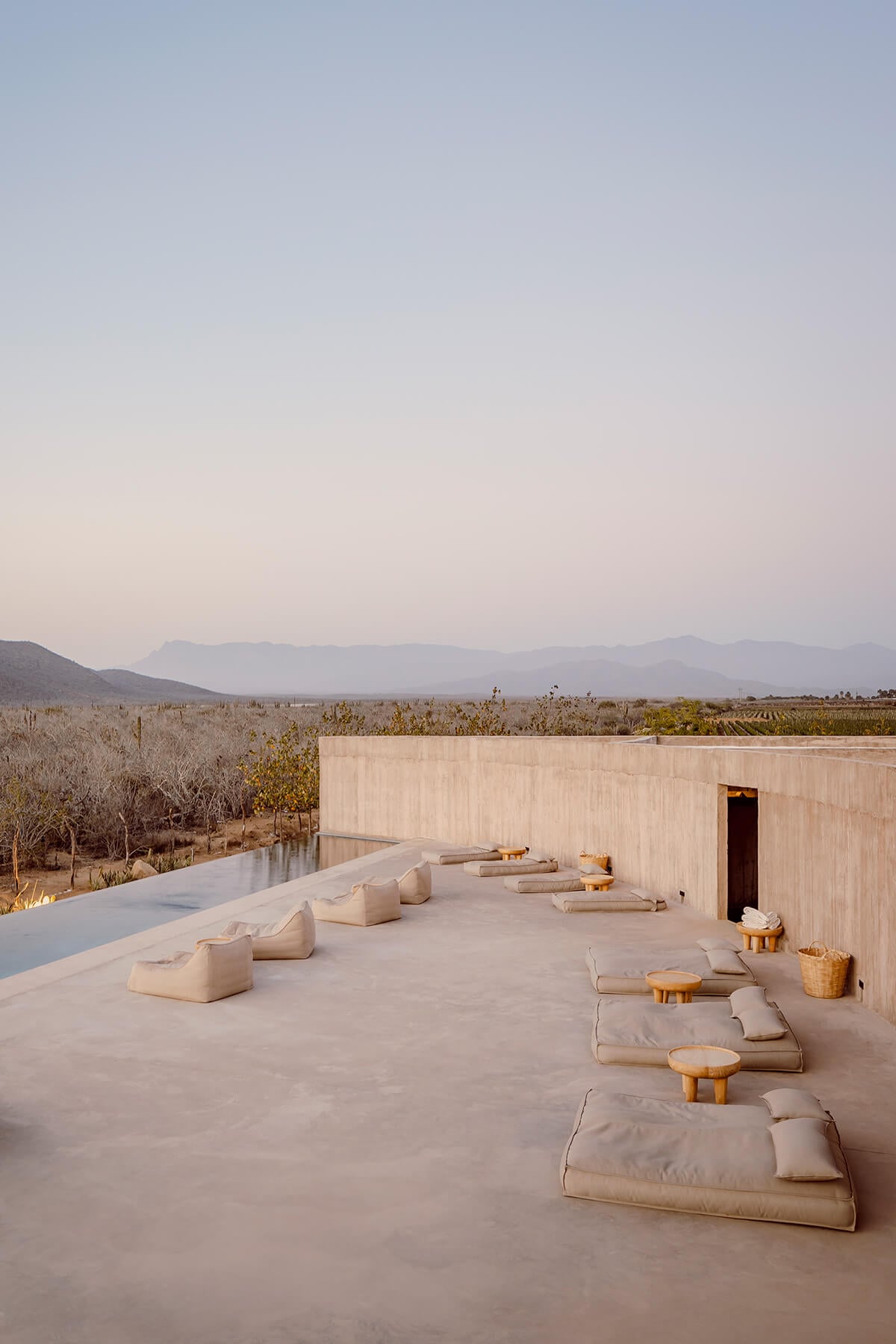 Paradero Todos Santos, Mexico — Minimalist concrete terrace with linen loungers overlooking vineyards and mountains at sunset